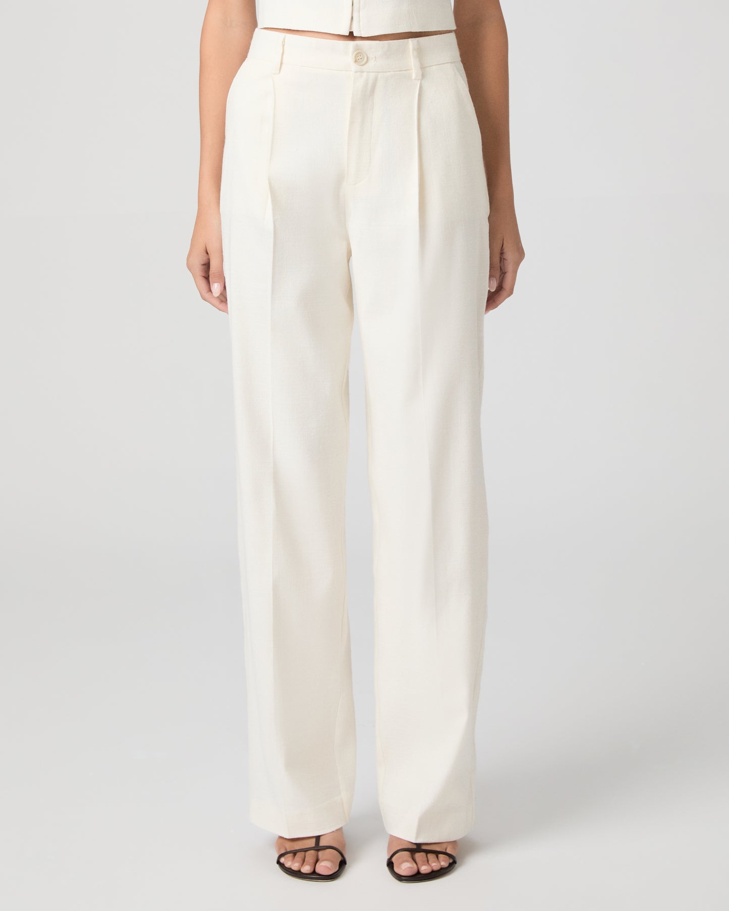 Woman wearing a white sleeveless top and pants on a plain background