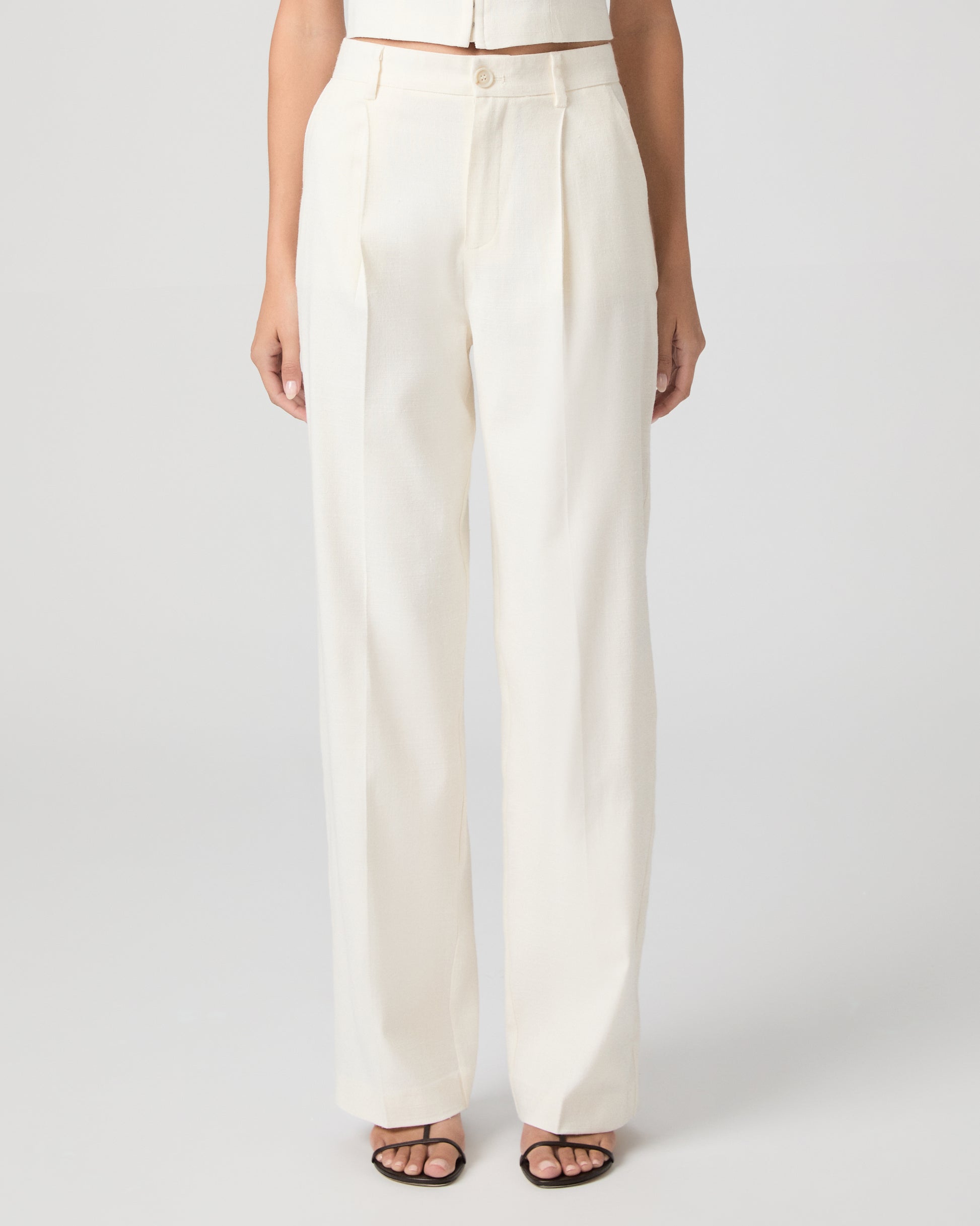 Woman wearing a white sleeveless top and pants on a plain background