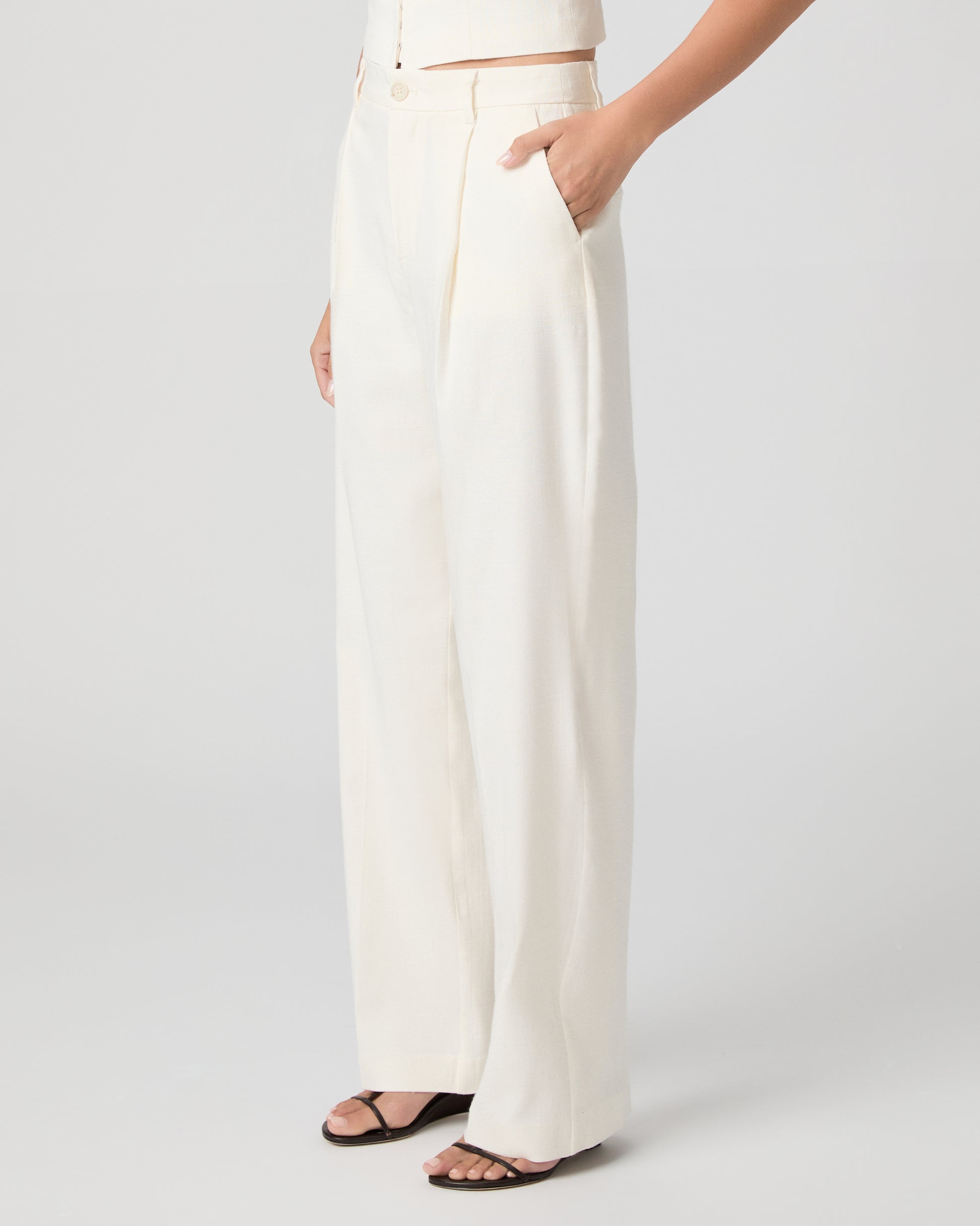 Woman wearing a white sleeveless top and pants on a plain background