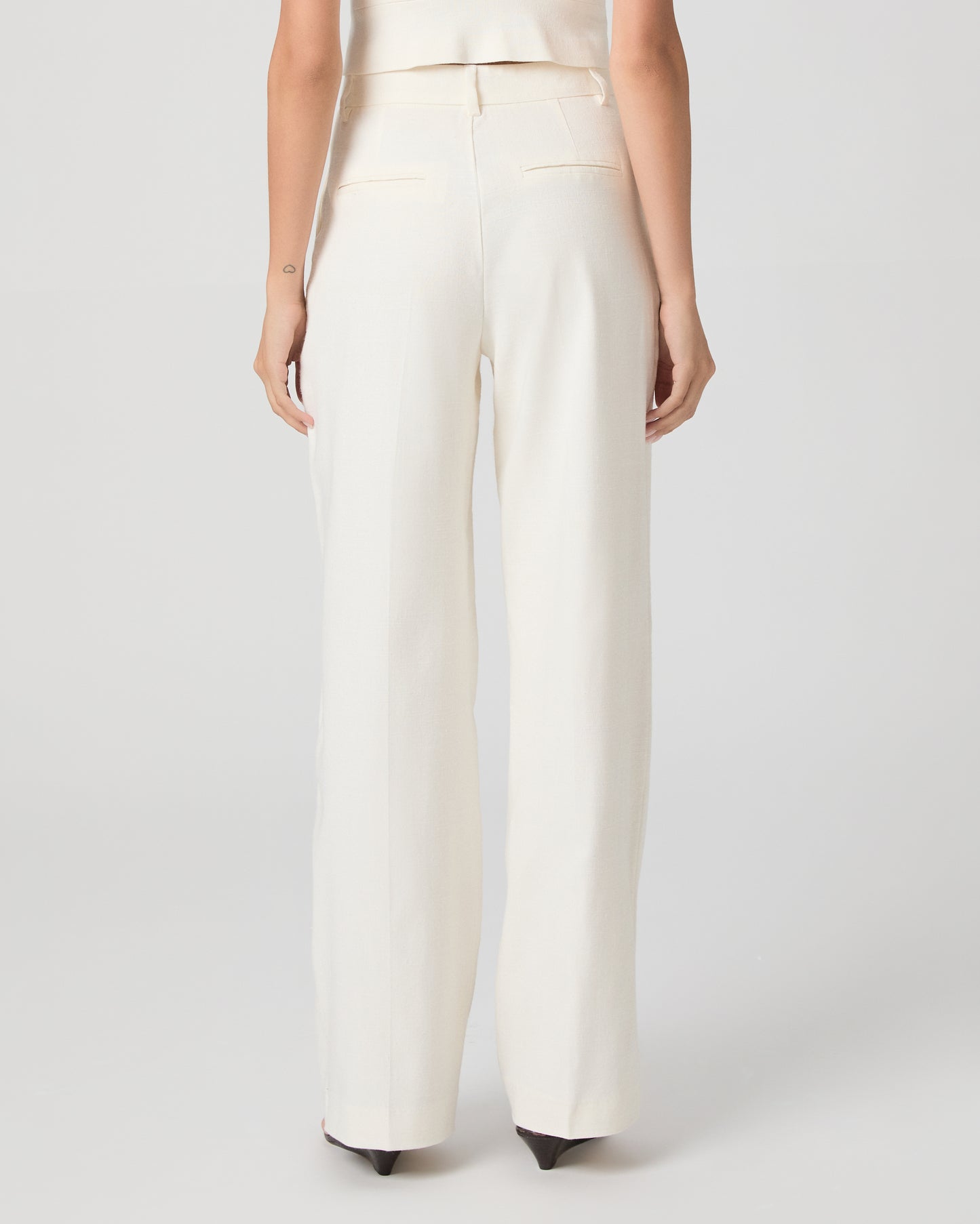Woman wearing a white sleeveless top and pants on a plain background