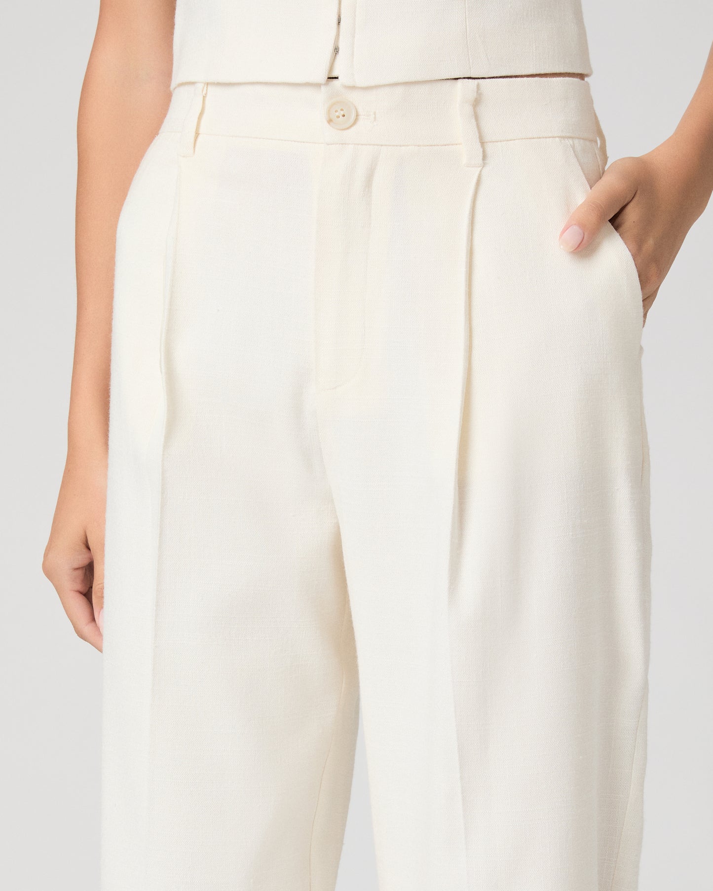 Woman wearing a white sleeveless top and pants on a plain background