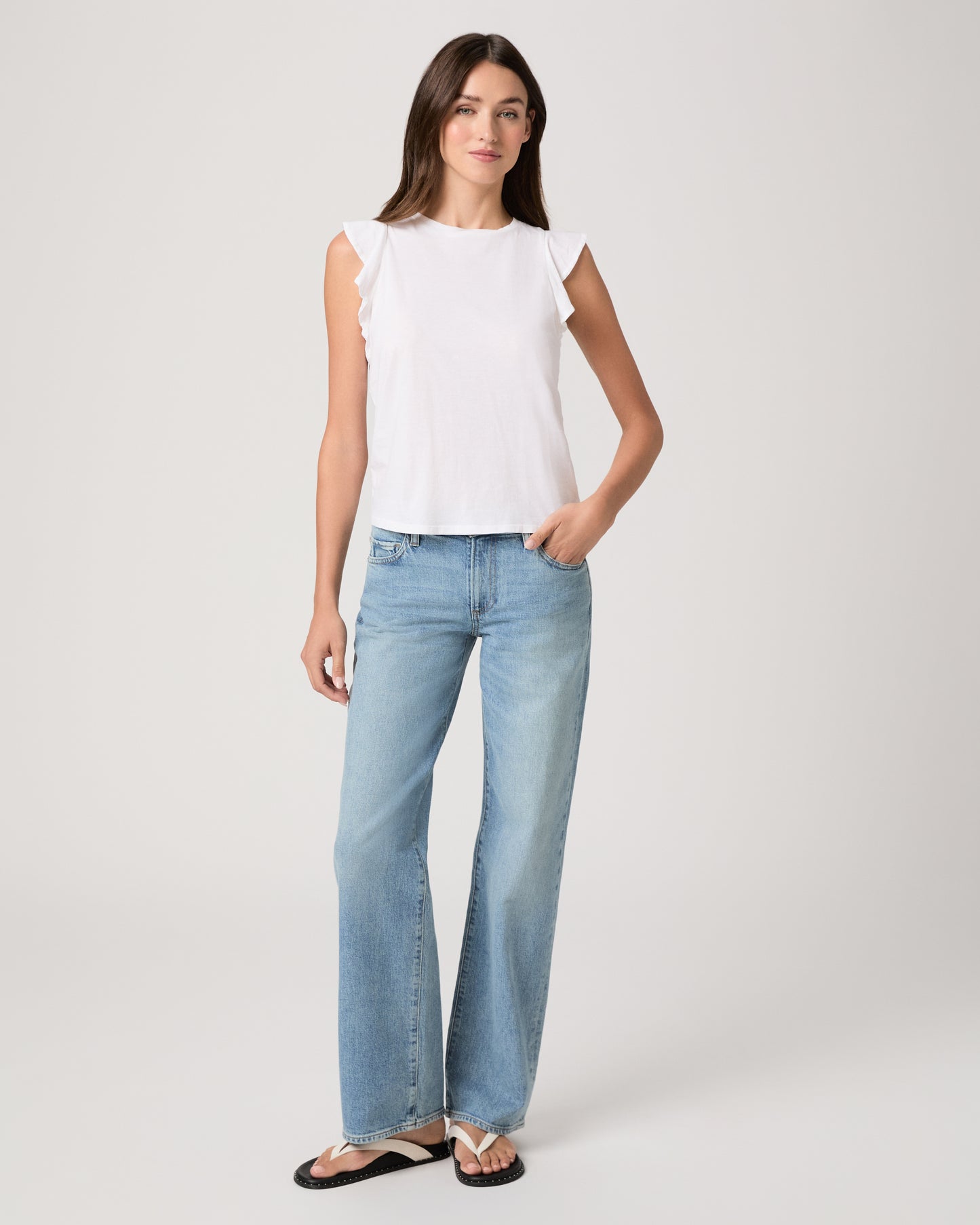 Model wearing a white tee paired with a light wash denim and white sandals