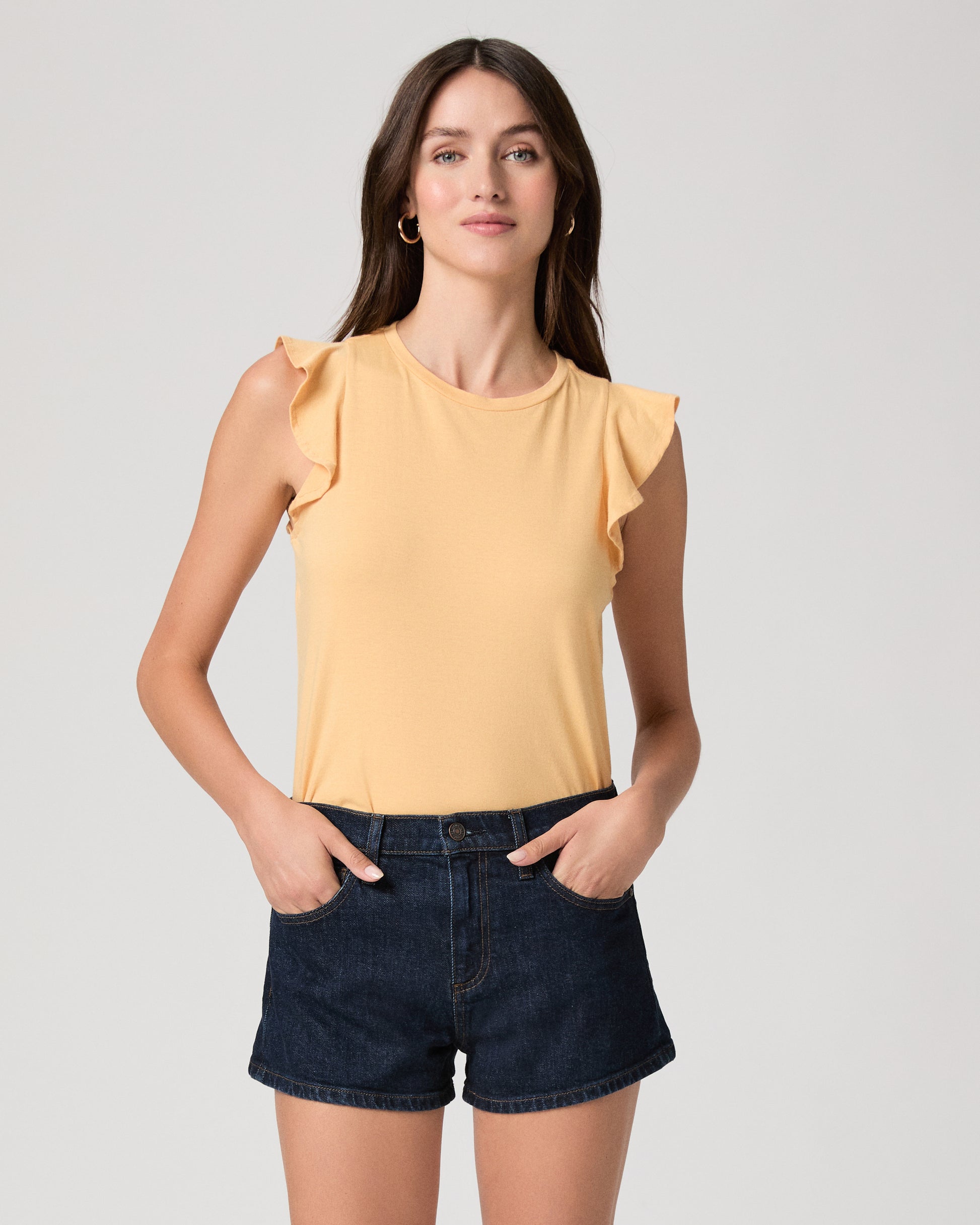 Woman wearing a yellow sleeveless top and denim shorts on a plain background