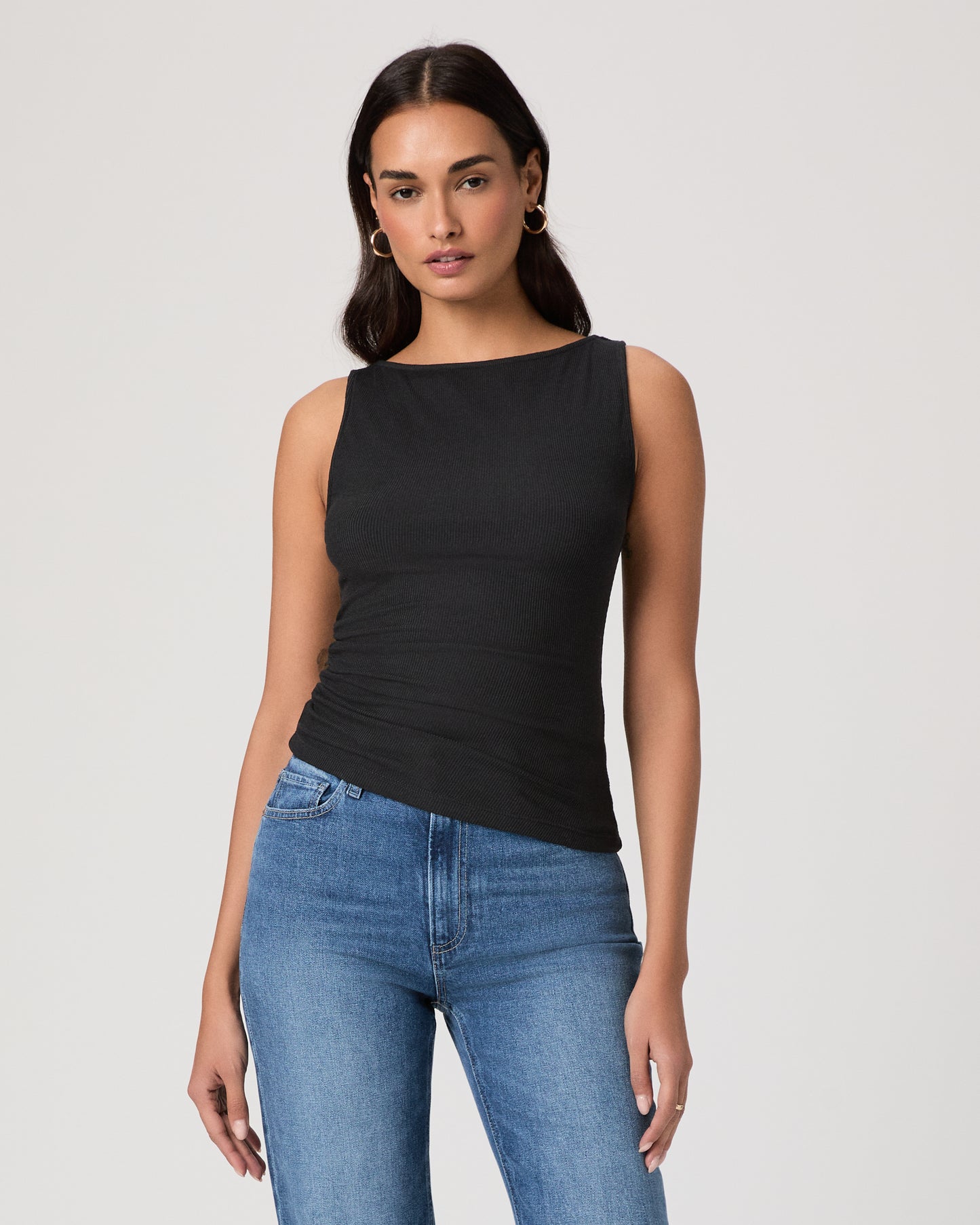 Woman wearing a black sleeveless top and blue jeans on a plain background