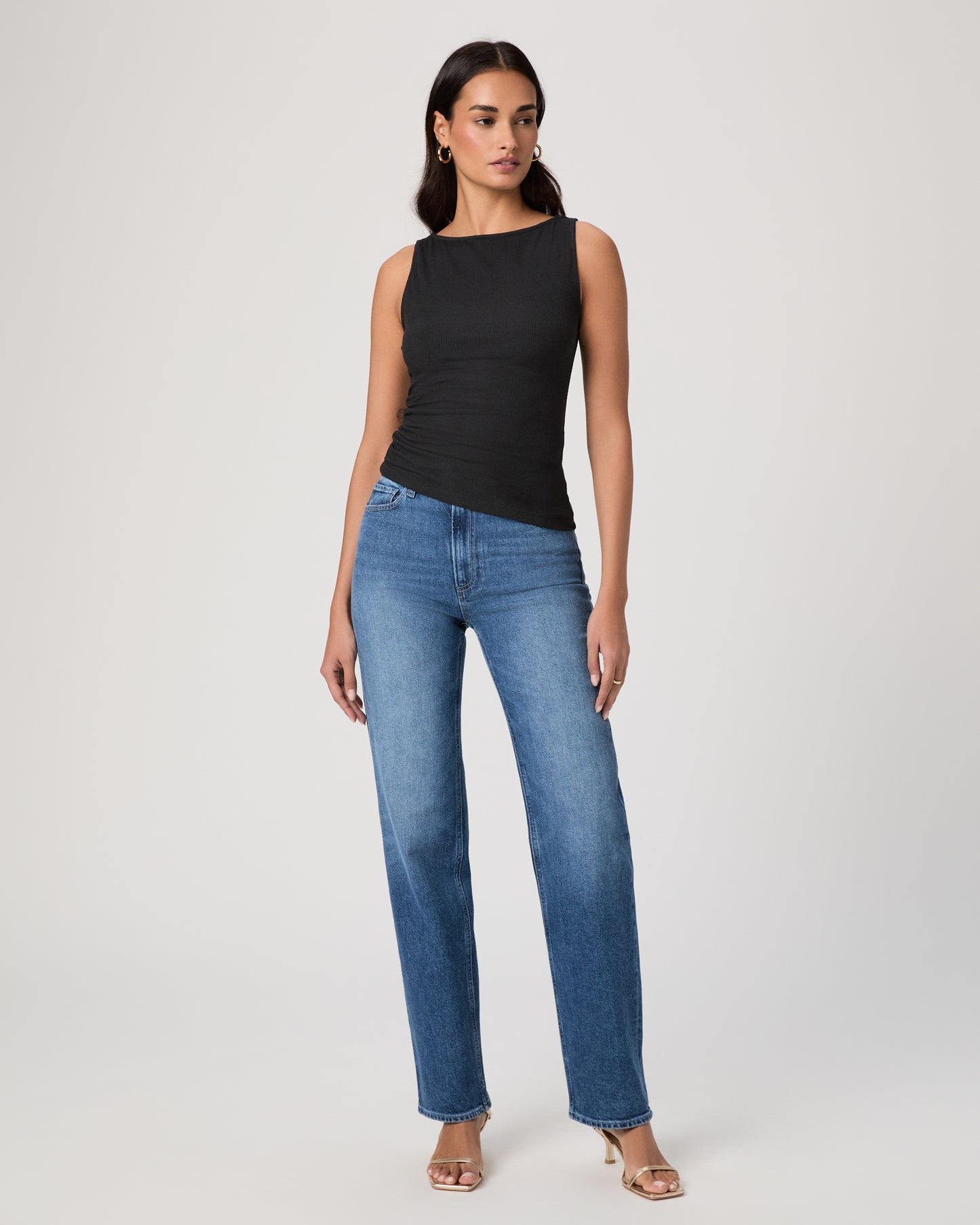 Woman wearing a black sleeveless top and blue jeans on a plain background
