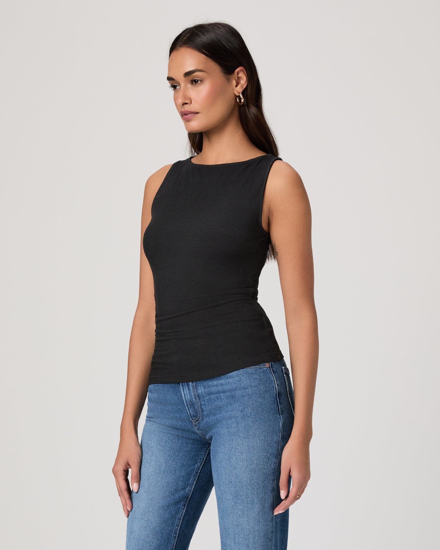 Woman wearing a black sleeveless top and blue jeans on a plain background