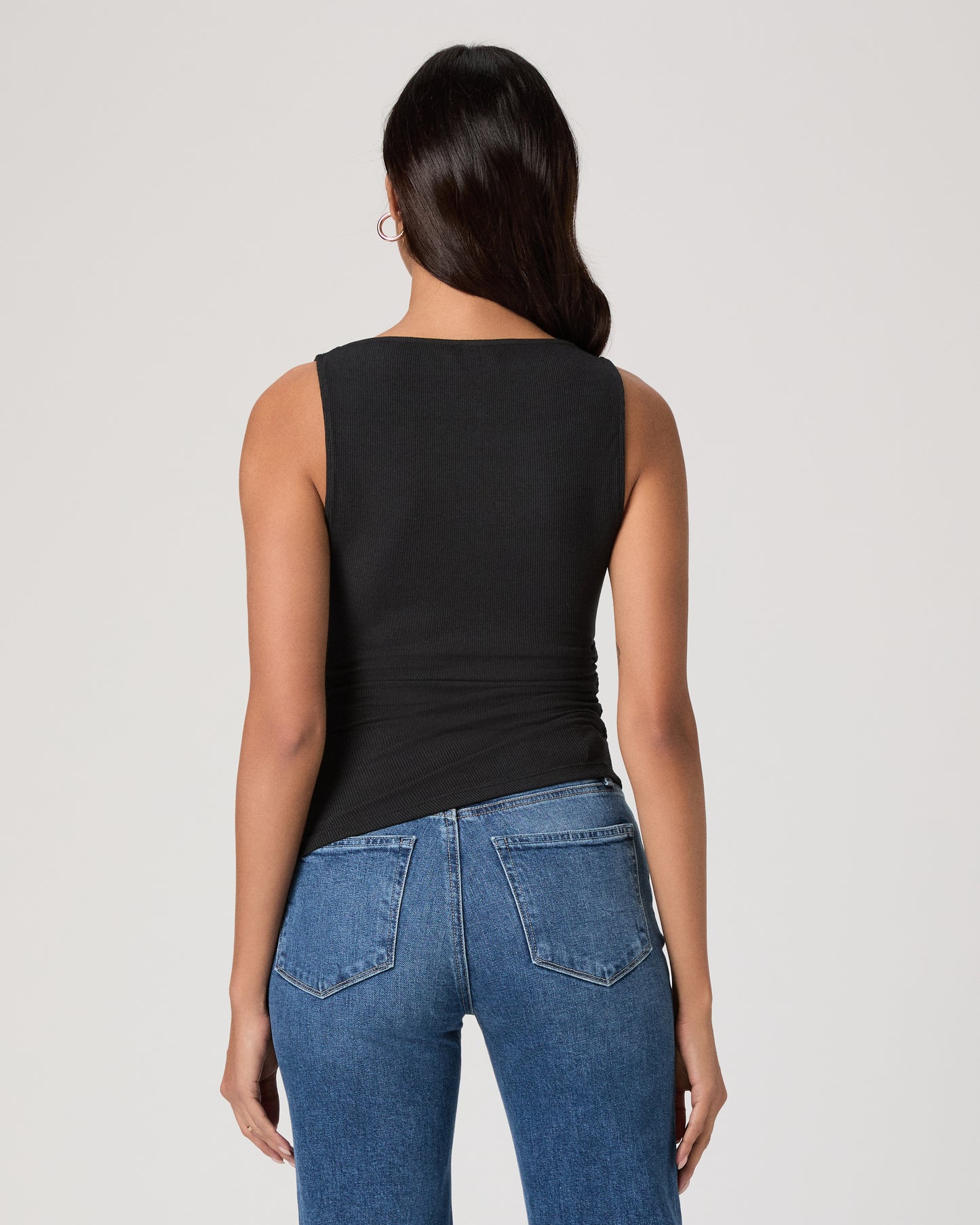 Woman wearing a black sleeveless top and blue jeans on a plain background