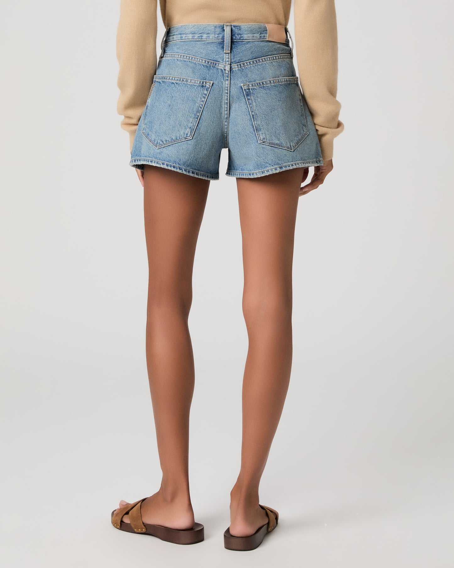 Woman wearing denim shorts and cream color long sleeve top on a plain background
