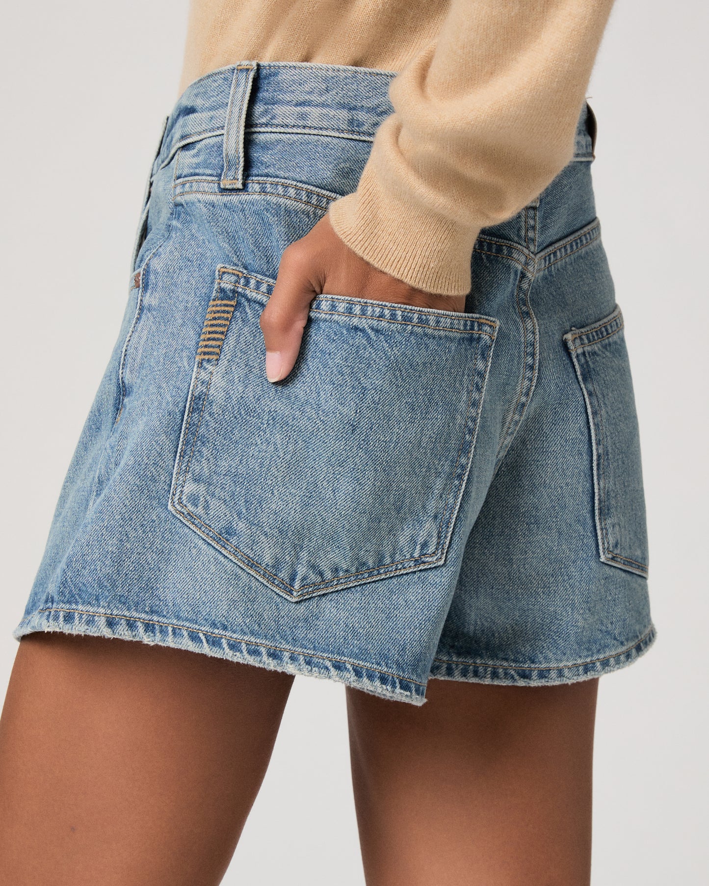 Woman wearing denim shorts and cream color long sleeve top on a plain background