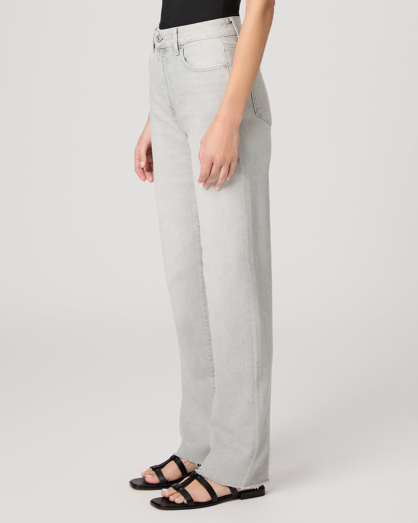 Woman wearing a black sleeveless top and light gray jeans paired with a black sandals on a white background