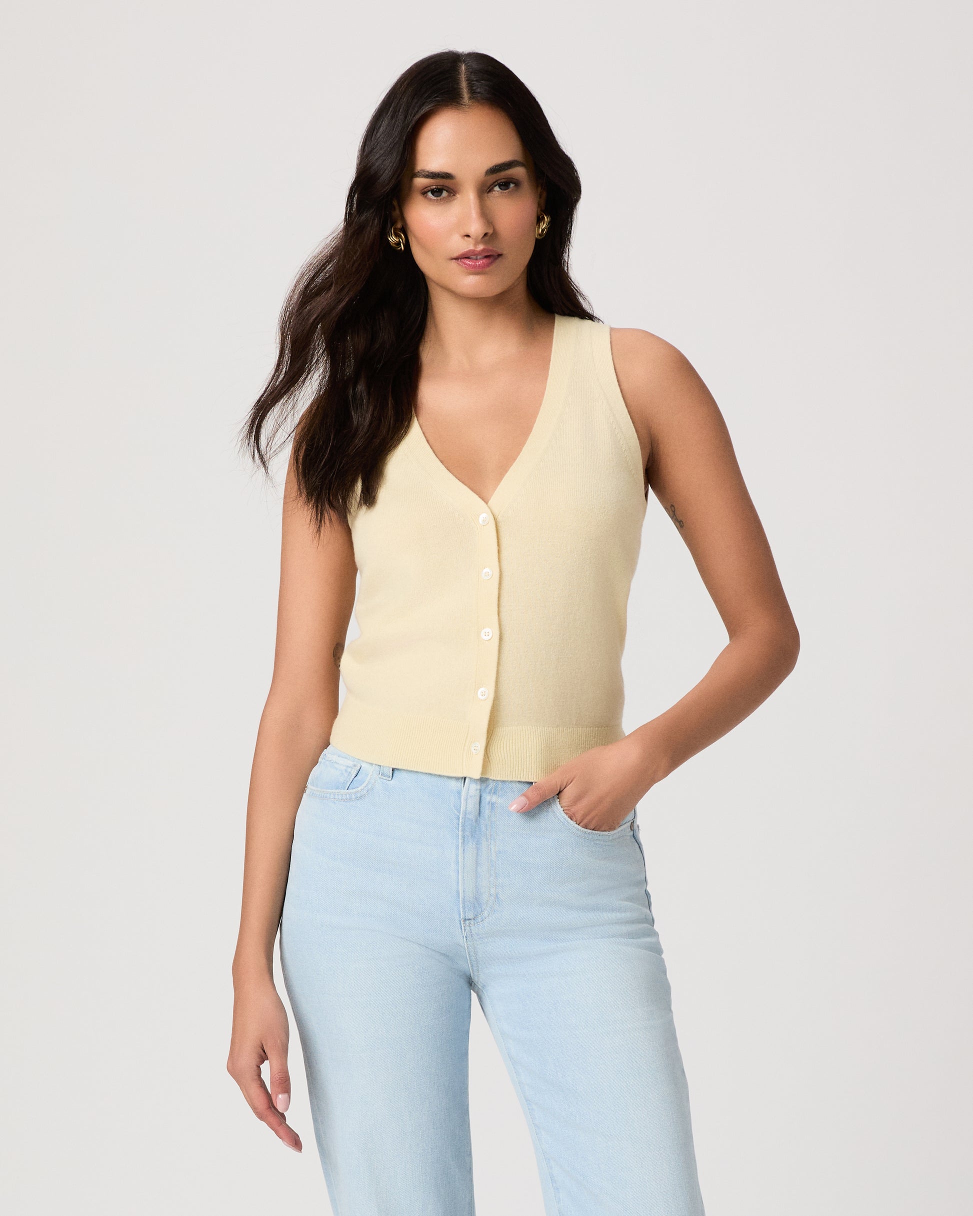 Woman wearing a light yellow sleeveless top and light blue jeans on a plain background