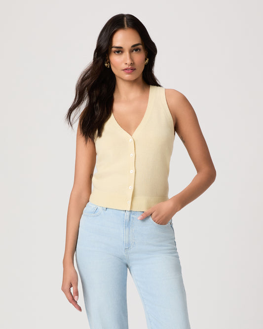 Woman wearing a light yellow sleeveless top and light blue jeans on a plain background