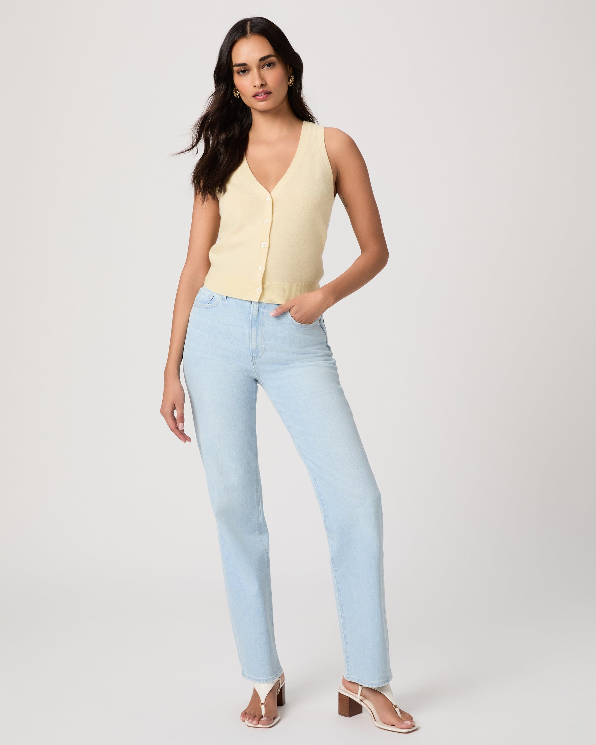 Woman wearing a light yellow sleeveless top and light blue jeans on a white background