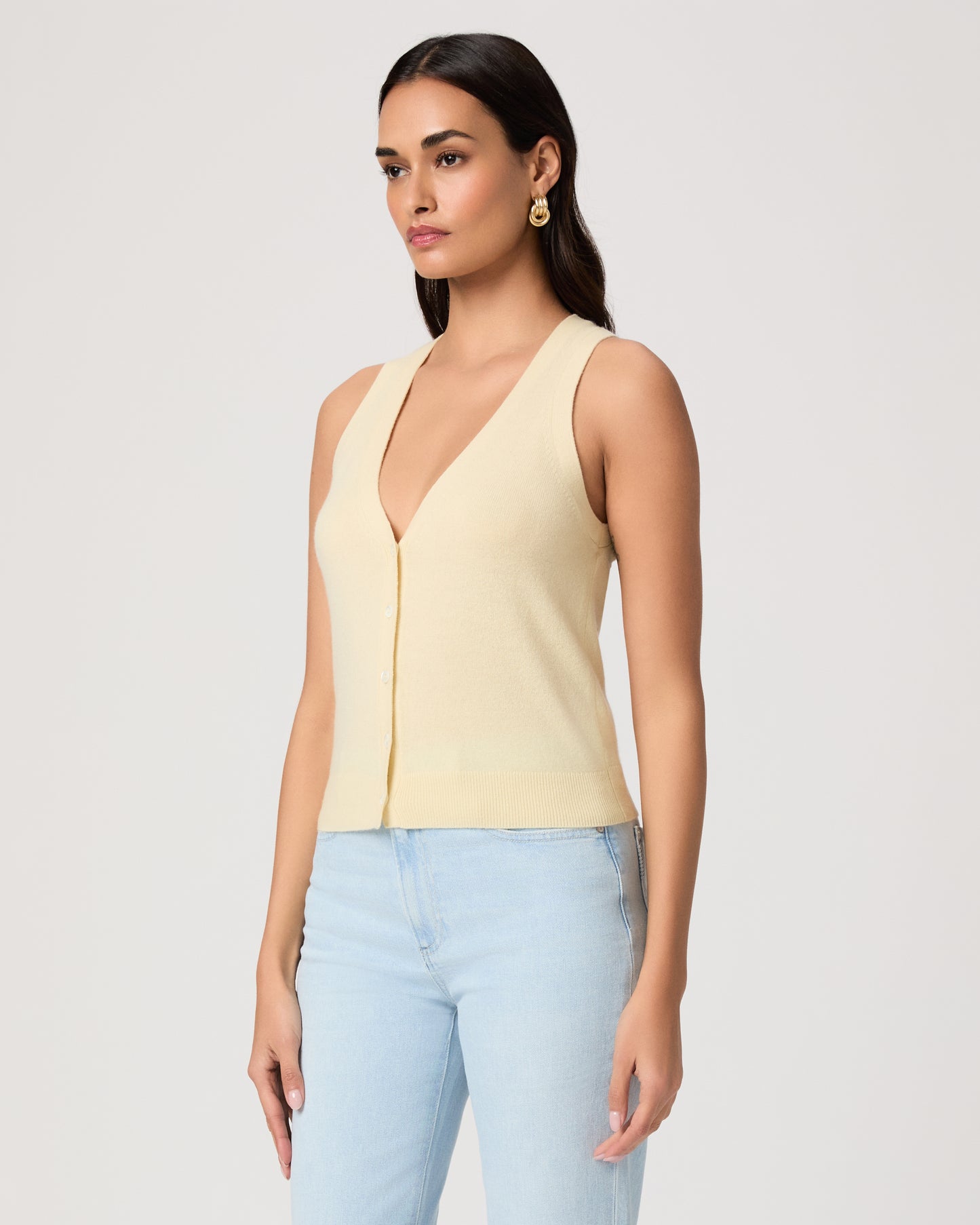 Woman wearing a light yellow sleeveless top and light blue jeans on a plain background