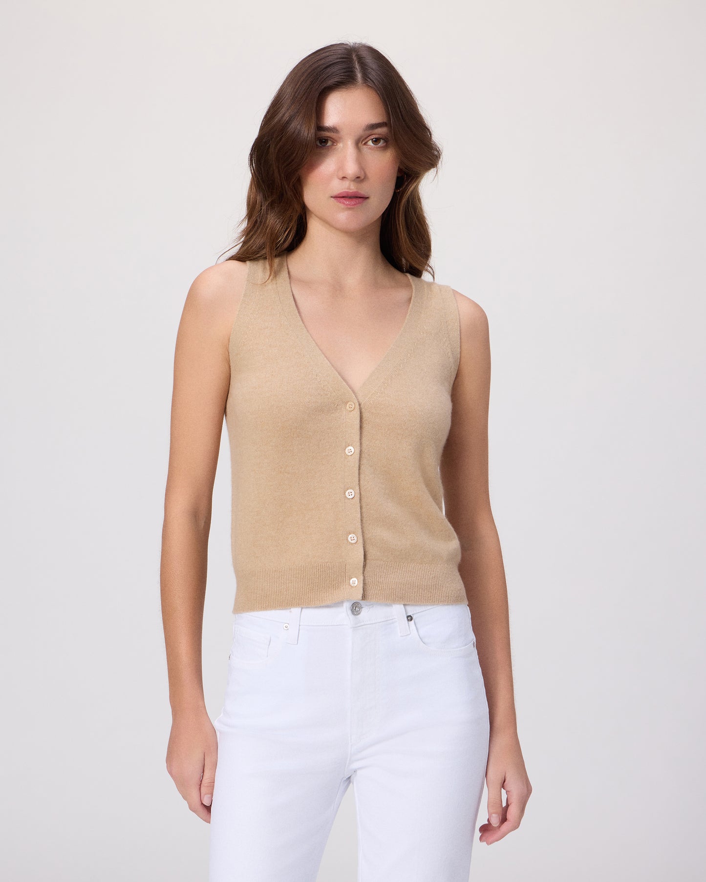 Woman wearing a beige sleeveless top with white pants on a light gray background