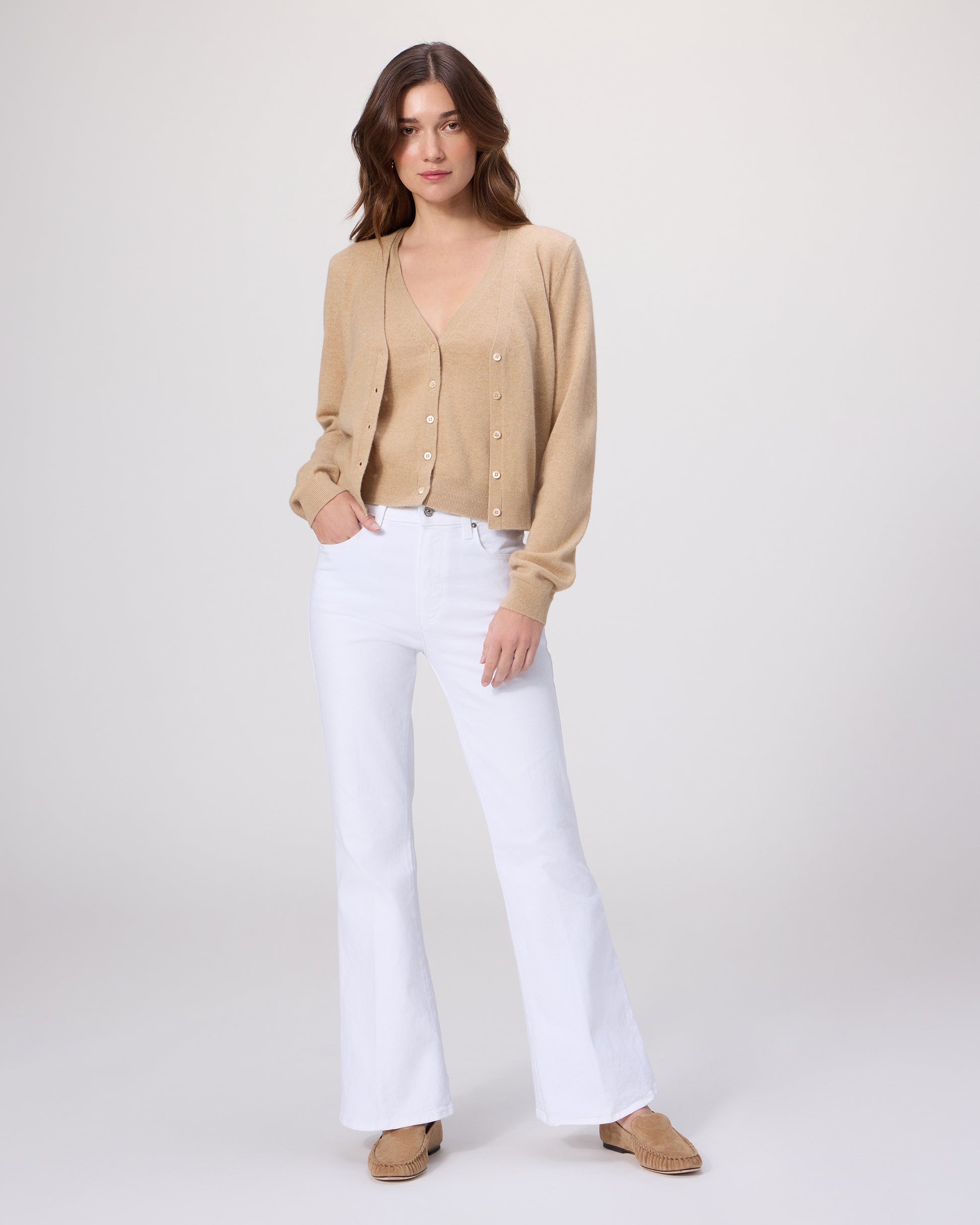 Woman wearing a beige Sweater top with white pants on a light gray background
