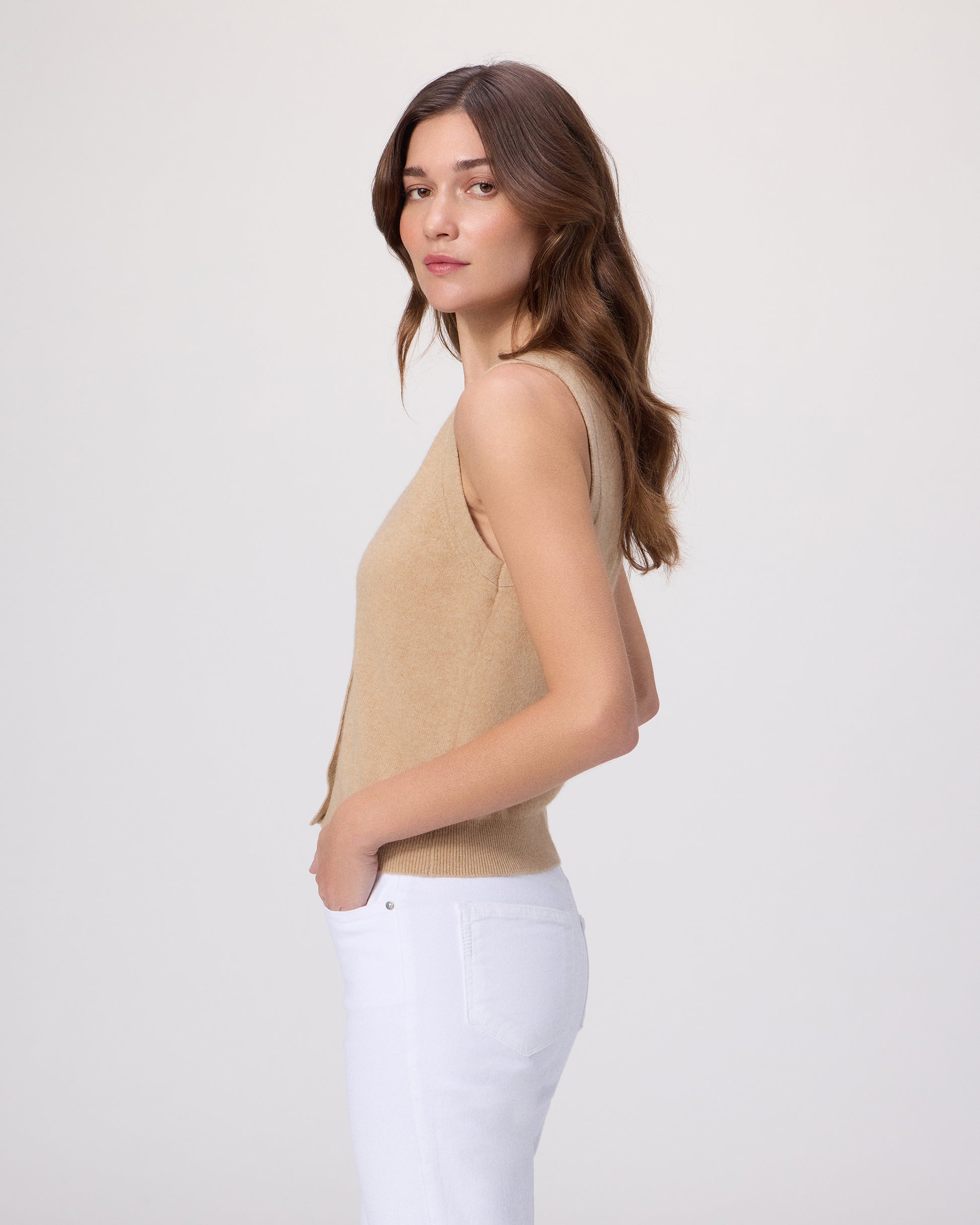 Woman wearing a beige sleeveless top with white pants on a light gray background