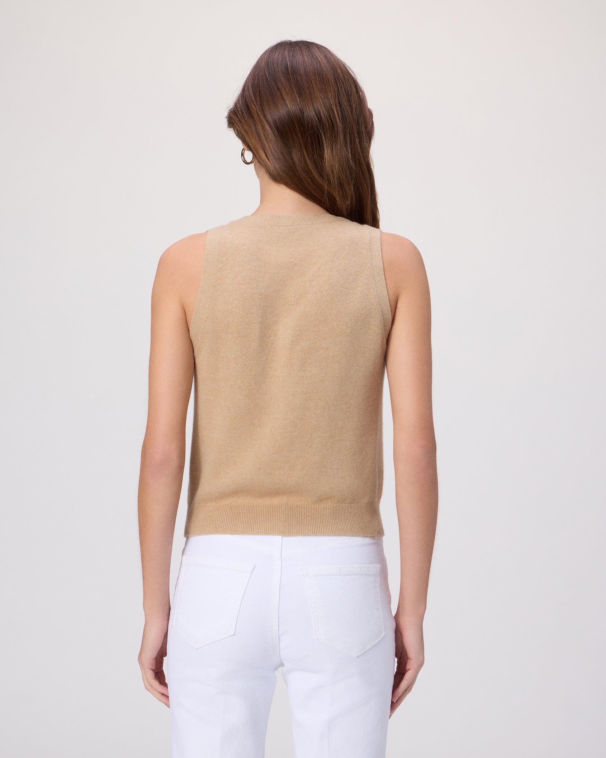 Woman wearing a beige sleeveless top with white pants on a light gray background