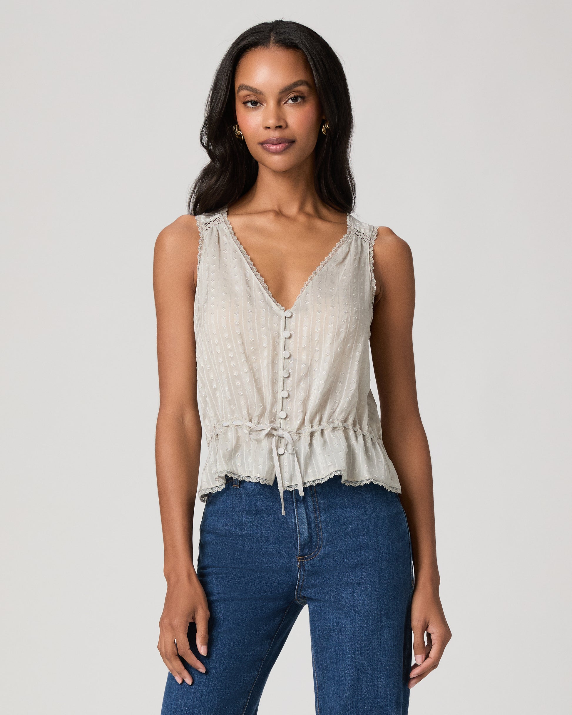 Woman wearing a light blue sleeveless top and blue jeans on a plain background