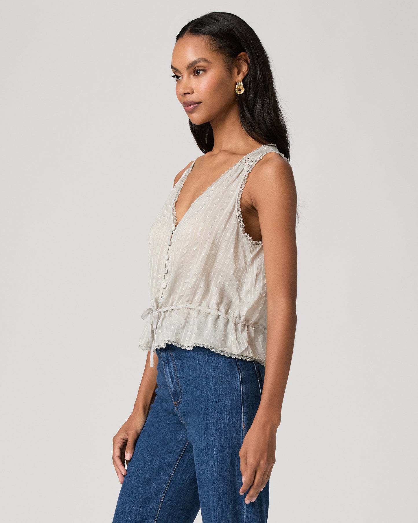 Woman wearing a light blue sleeveless top and blue jeans on a plain background