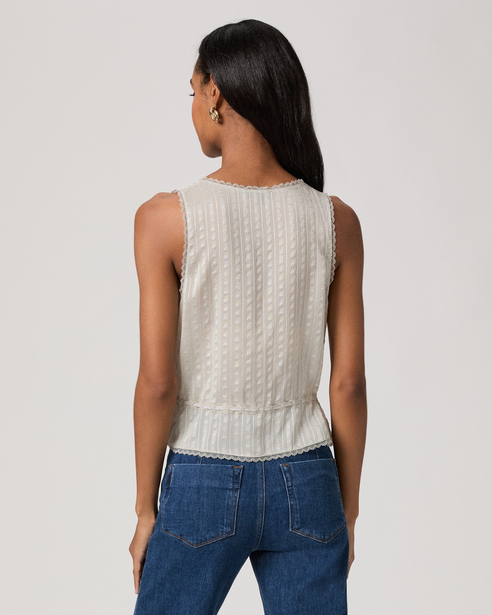Woman wearing a light blue sleeveless top and blue jeans on a plain background