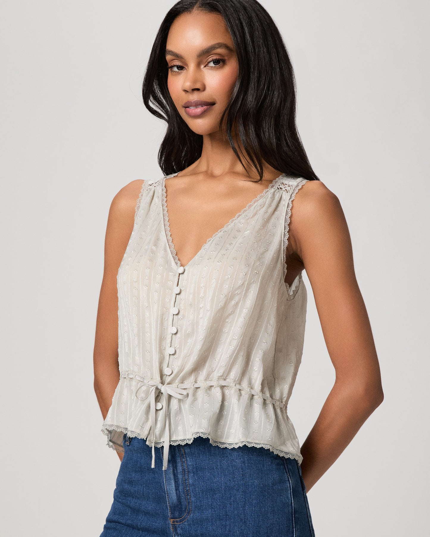Woman wearing a light blue sleeveless top and blue jeans on a plain background