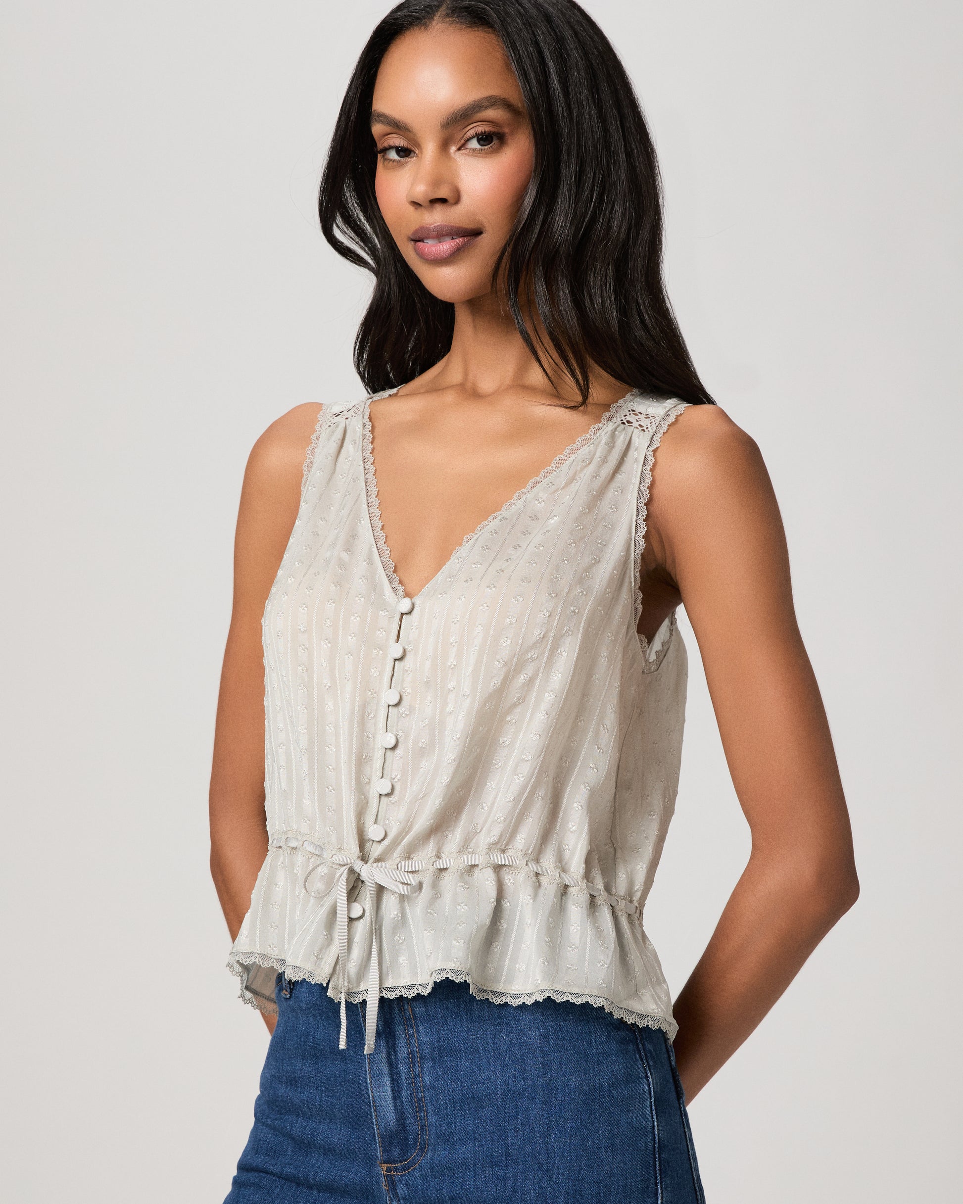 Woman wearing a light blue sleeveless top and blue jeans on a plain background