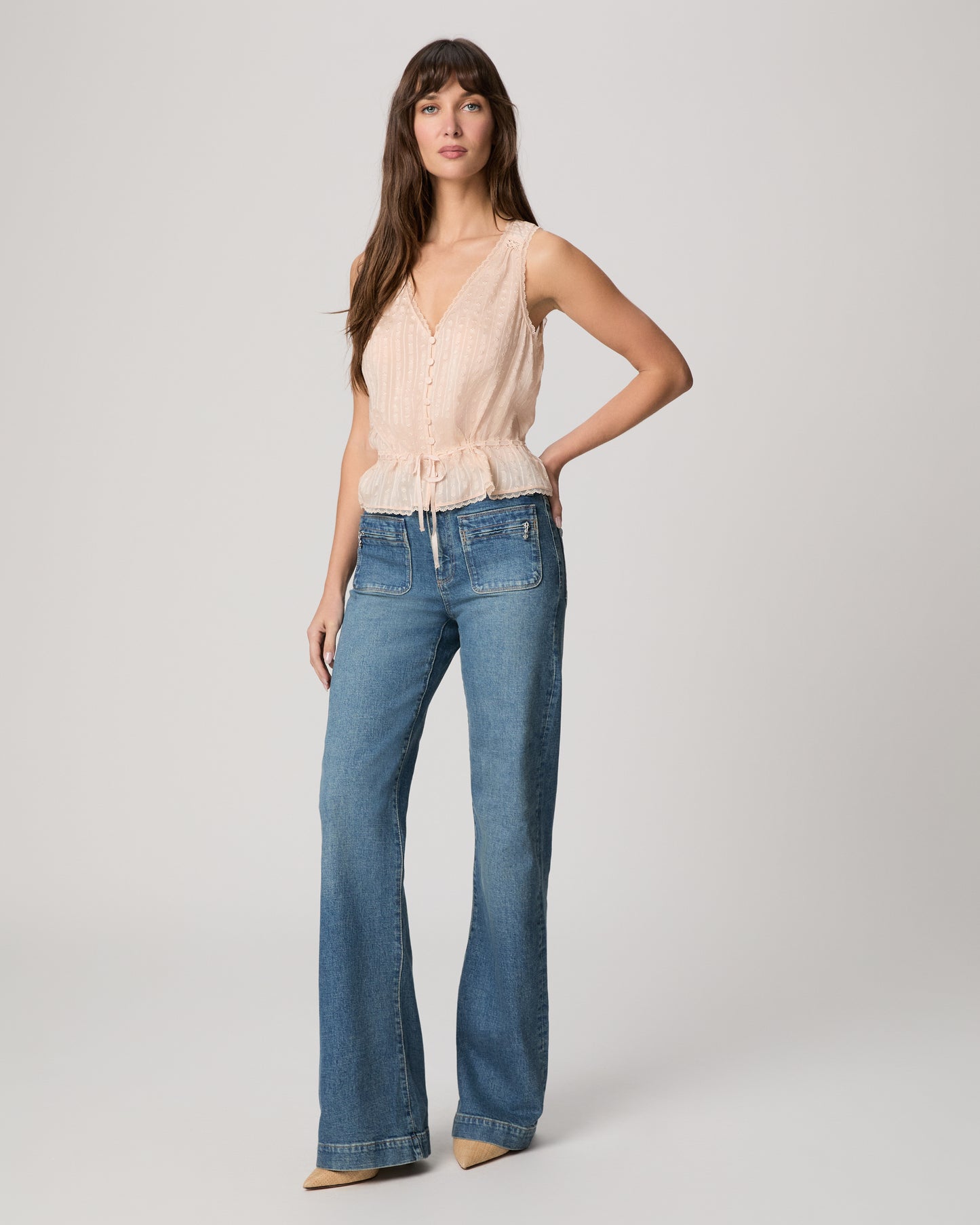 Woman wearing a light pink sleeveless top and blue jeans on a plain background
