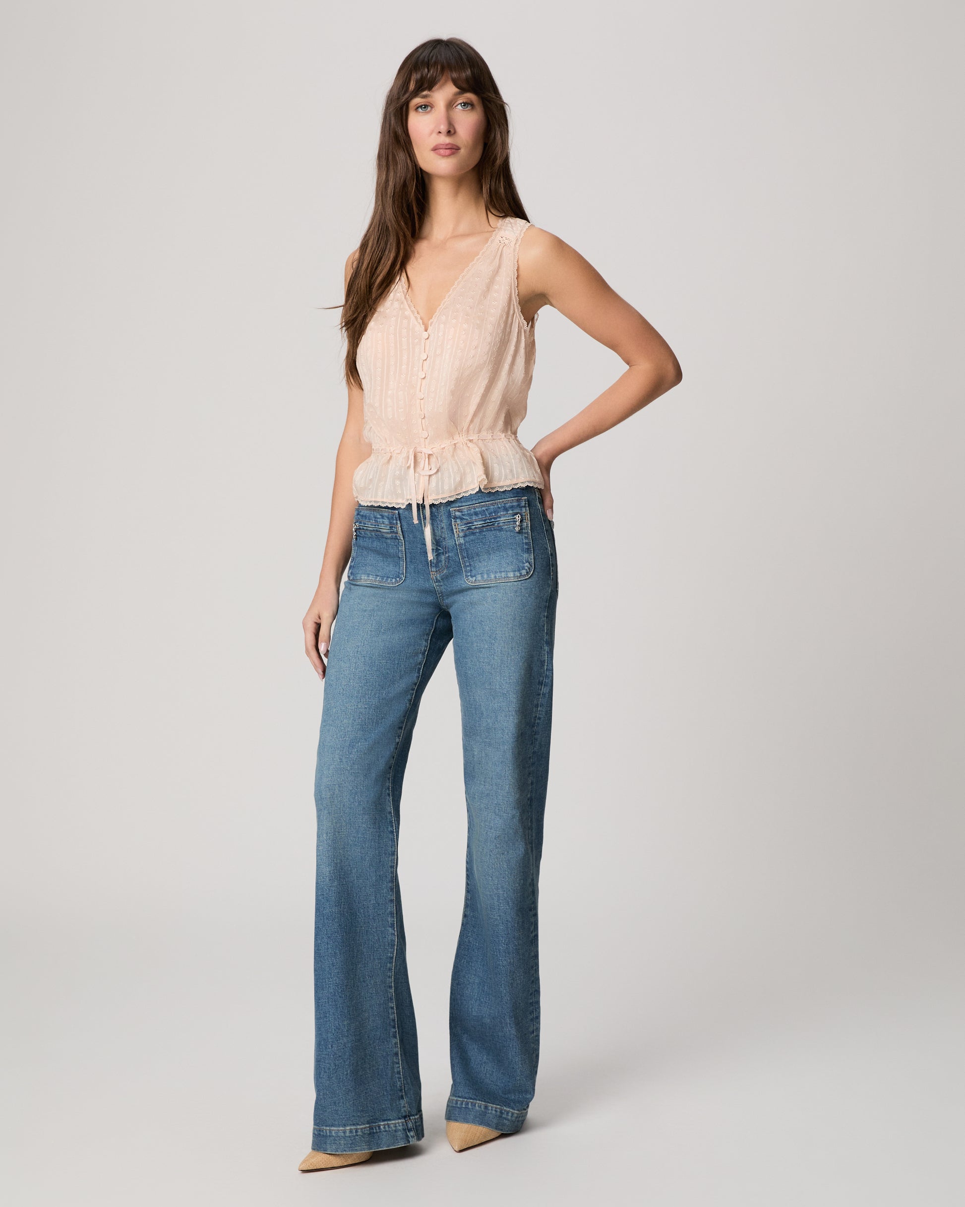Woman wearing a light pink sleeveless top and blue jeans on a plain background