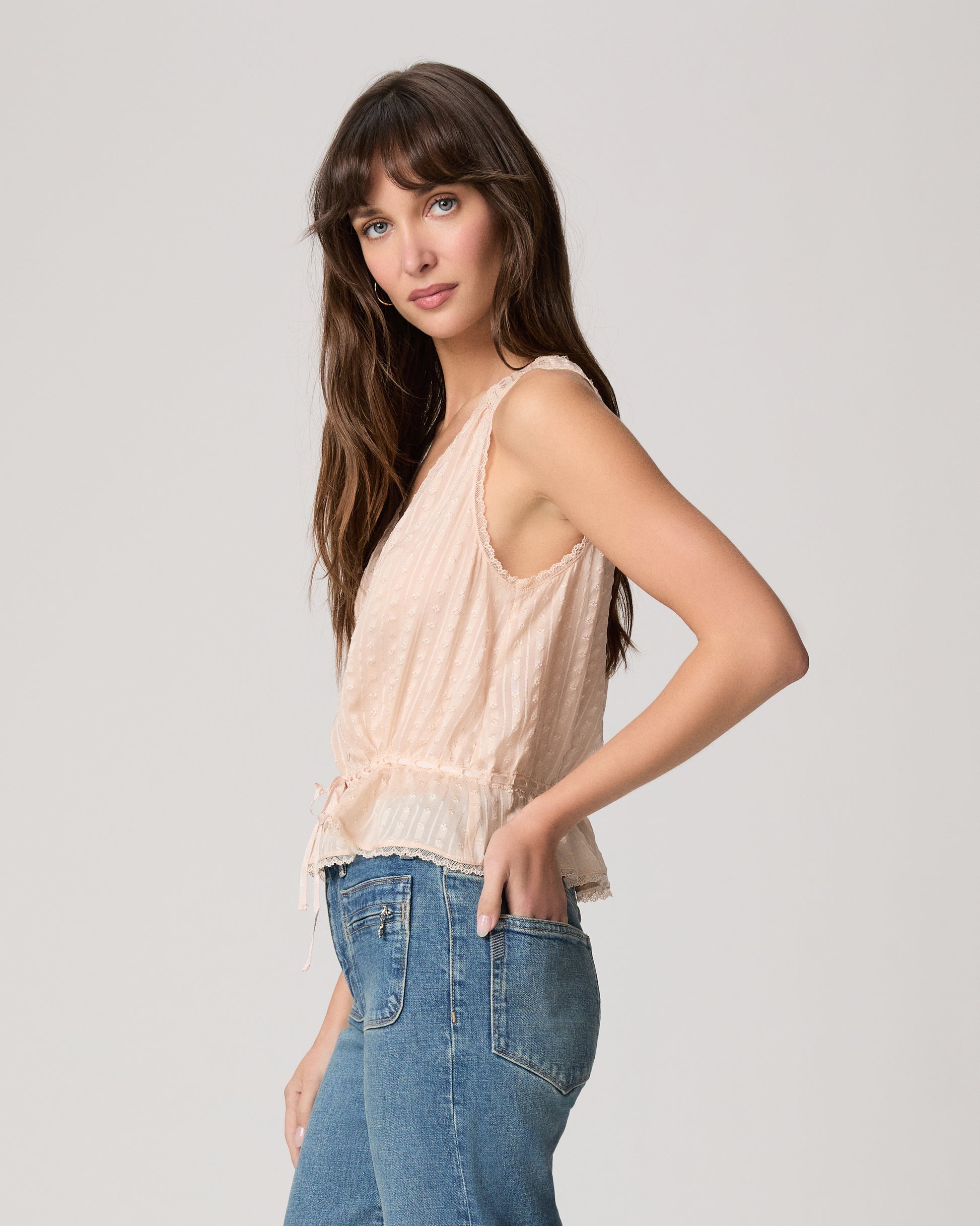 Woman wearing a light pink sleeveless top and blue jeans on a plain background