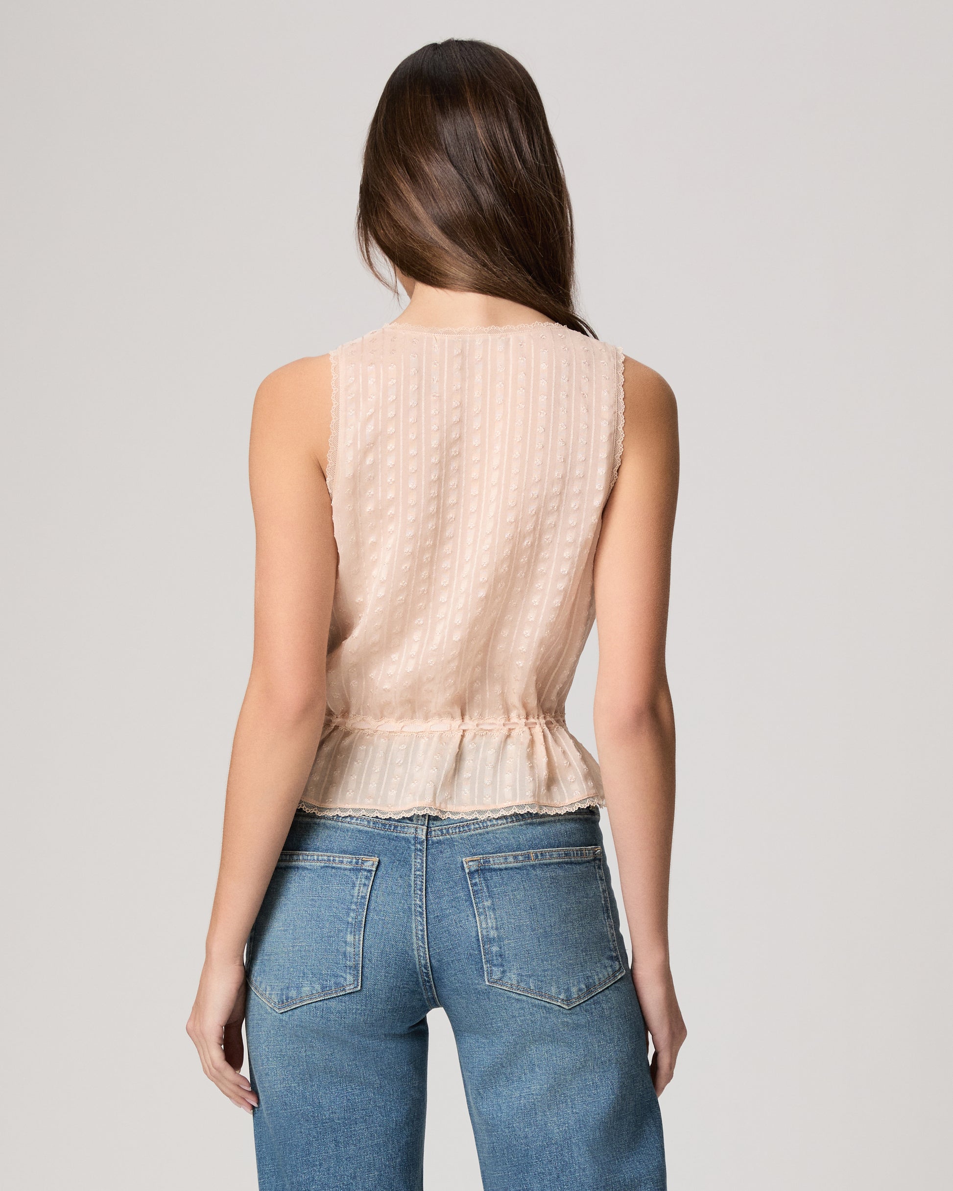 Woman wearing a light pink sleeveless top and blue jeans on a plain background
