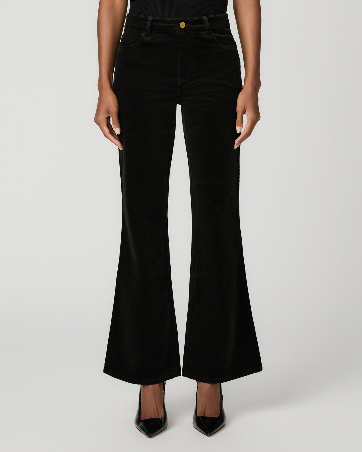 Close-up front view of black corduroy flare pants with a button waistband, paired with black pointed-toe heels.