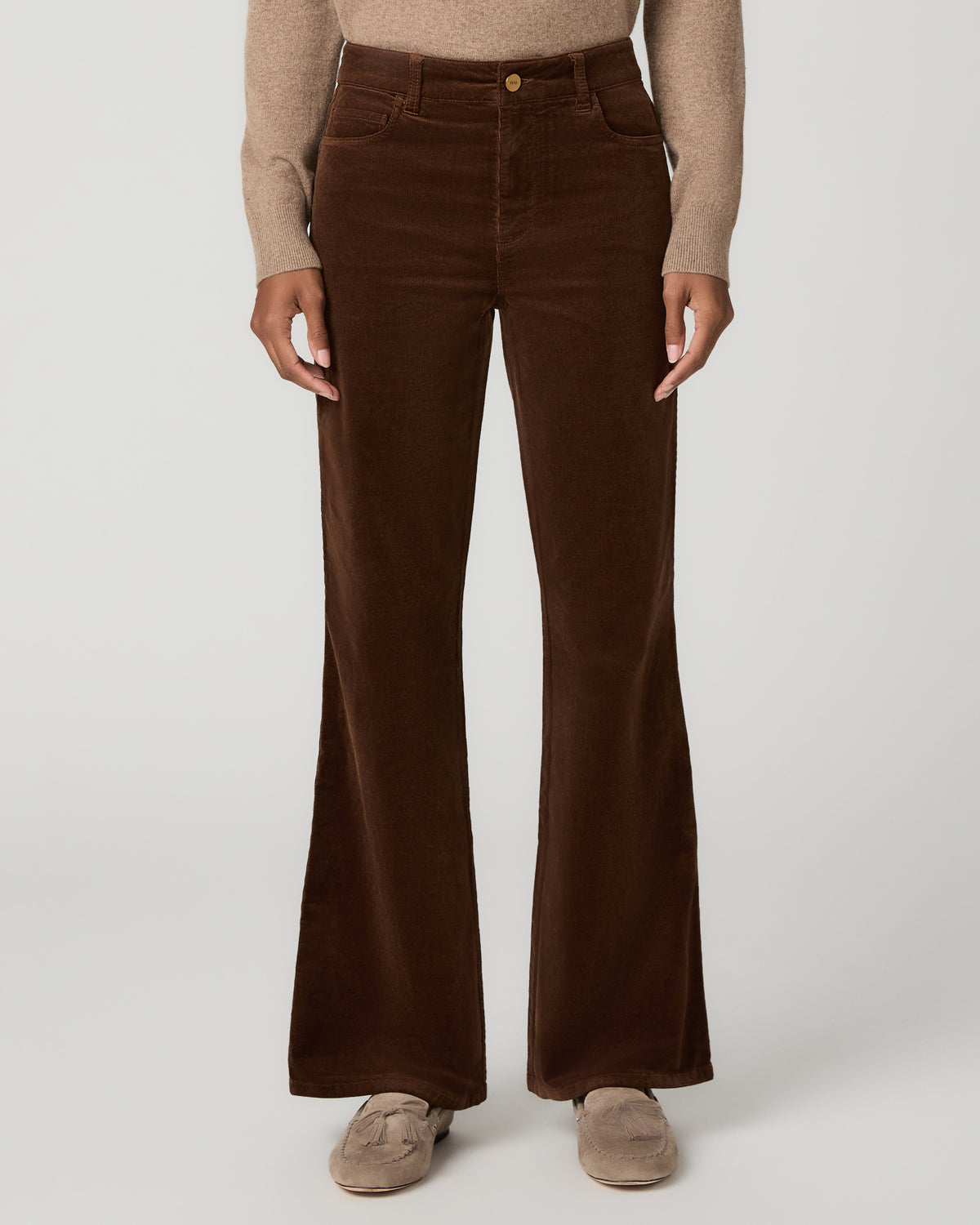 Close-up front view of hickory brown corduroy flare pants with a button waistband, styled with a tan turtleneck sweater and tan flats.