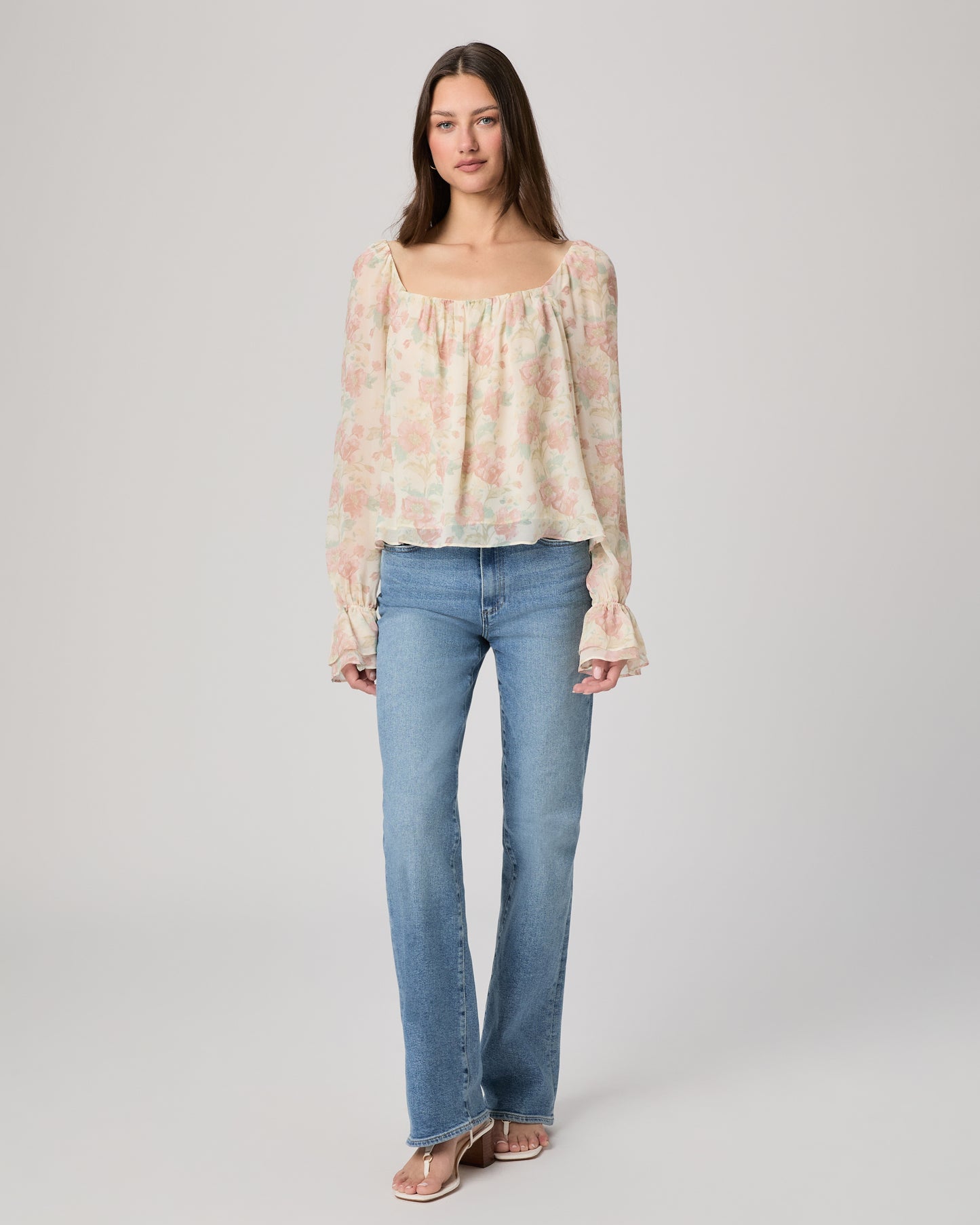 Woman wearing a floral blouse and jeans on a plain background