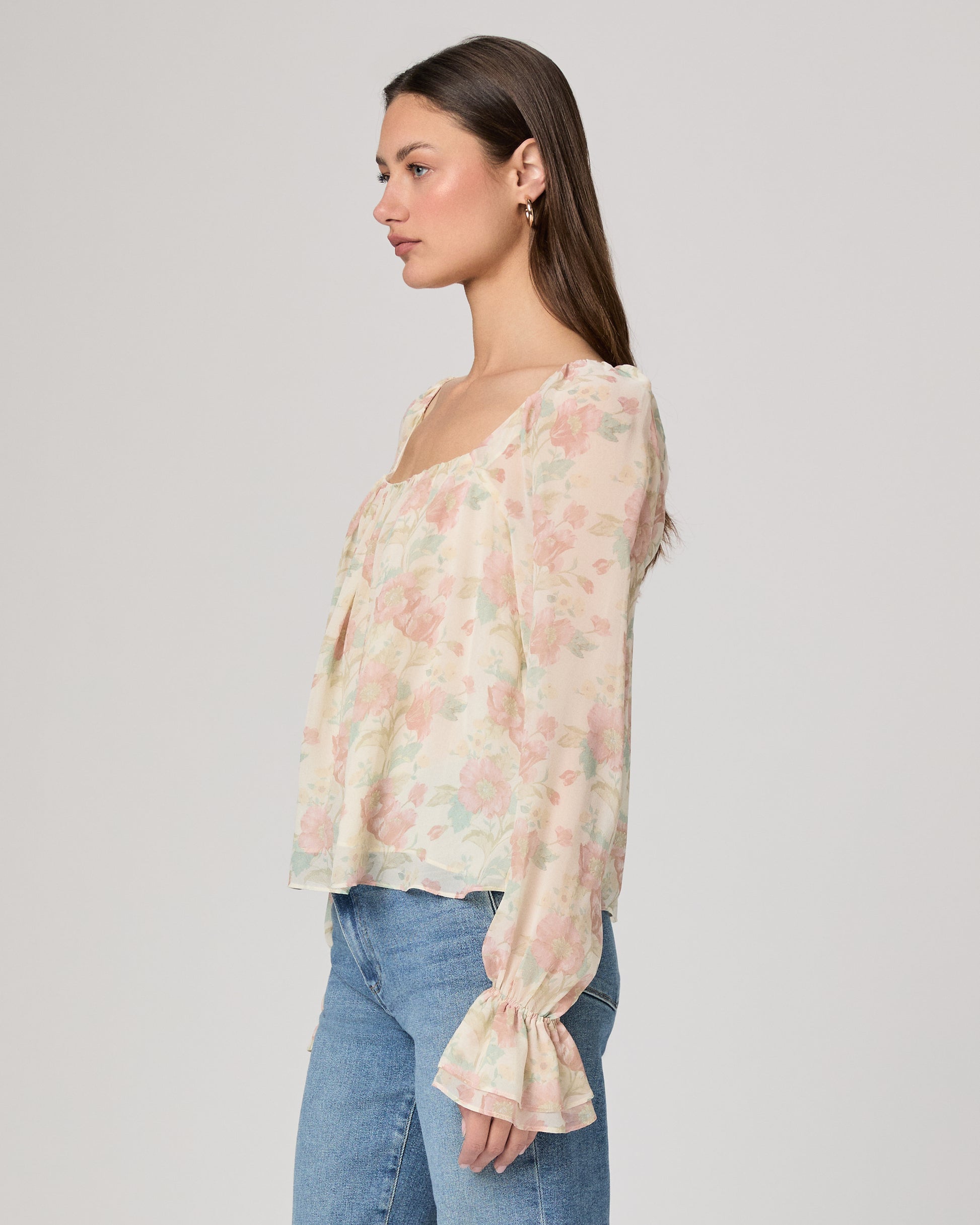 Woman wearing a floral blouse and jeans on a plain background