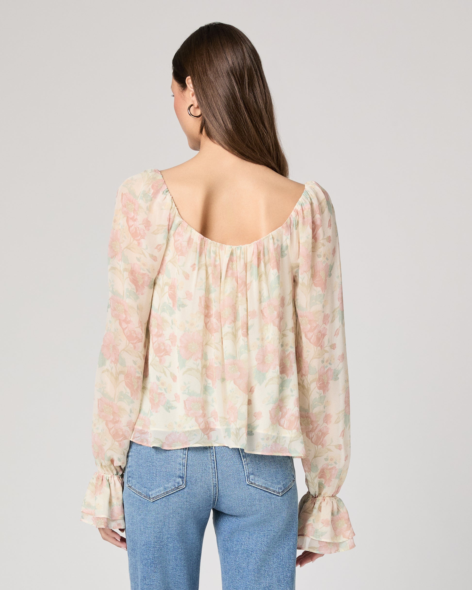 Woman wearing a floral blouse and jeans on a plain background