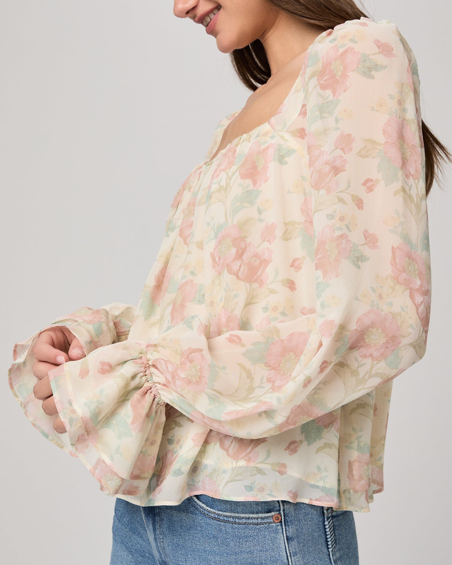 Woman wearing a floral blouse and jeans on a plain background