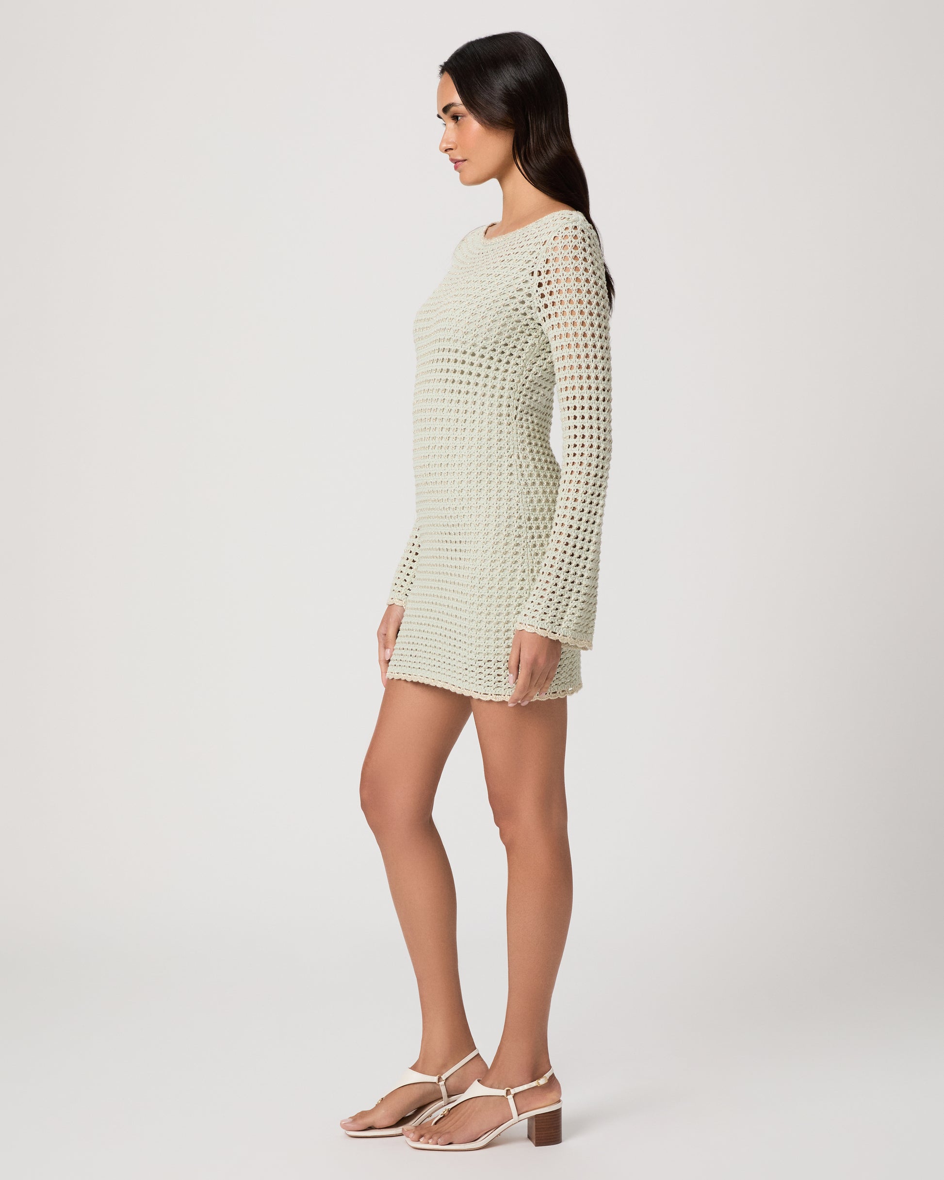 Woman wearing a light green knitted dress and white sandals on a white background