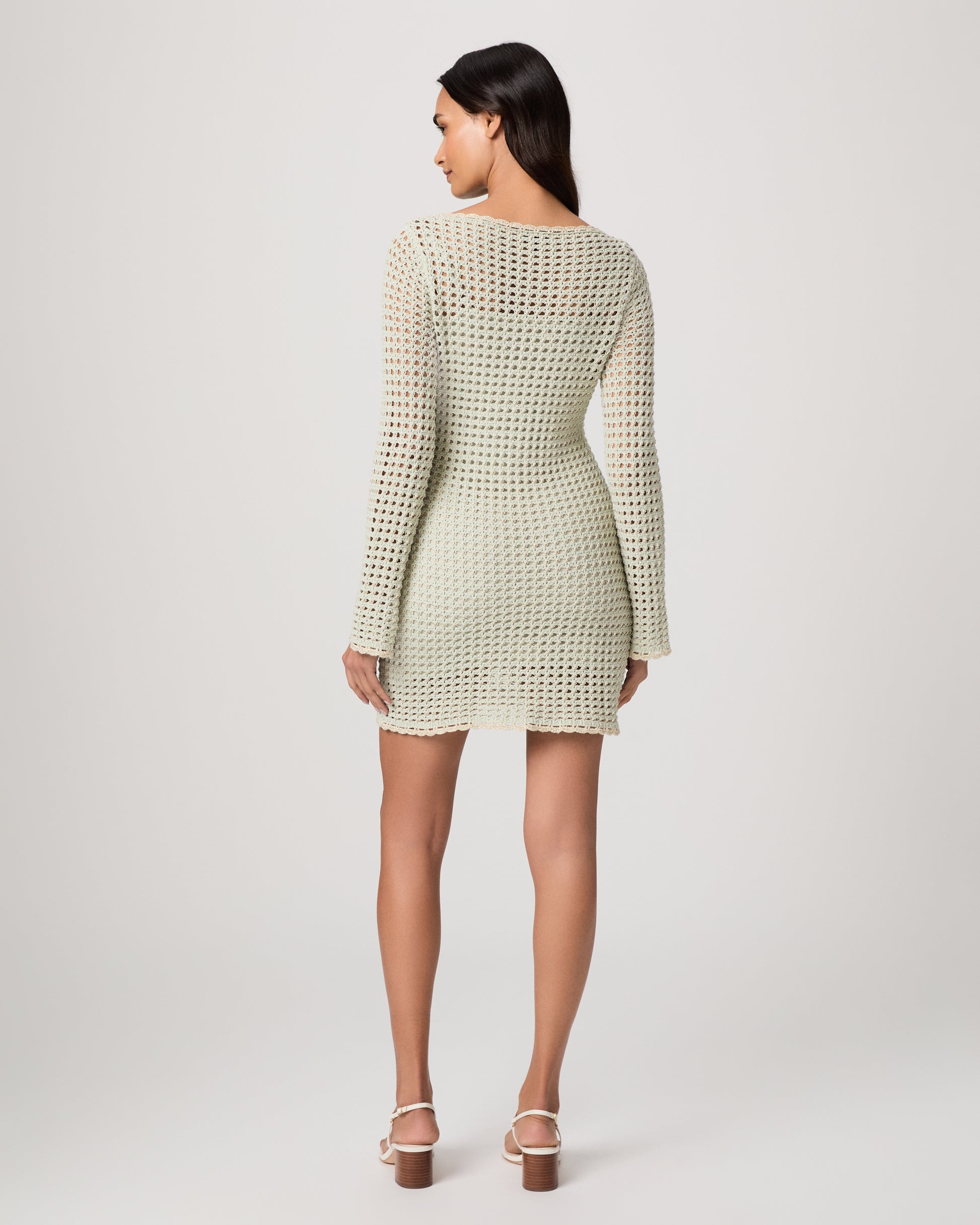 Woman wearing a light green knitted dress and white sandals on a white background