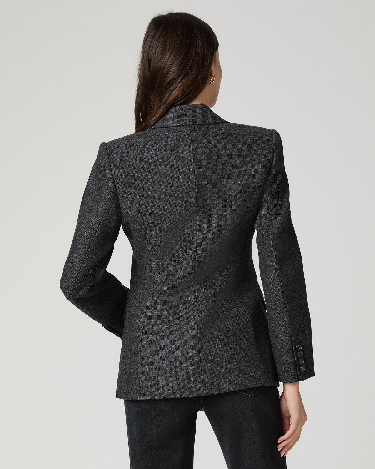 A woman modeling a dark gray textured blazer with dark charcoal flare jeans and a white tank top, standing against a light gray studio background.