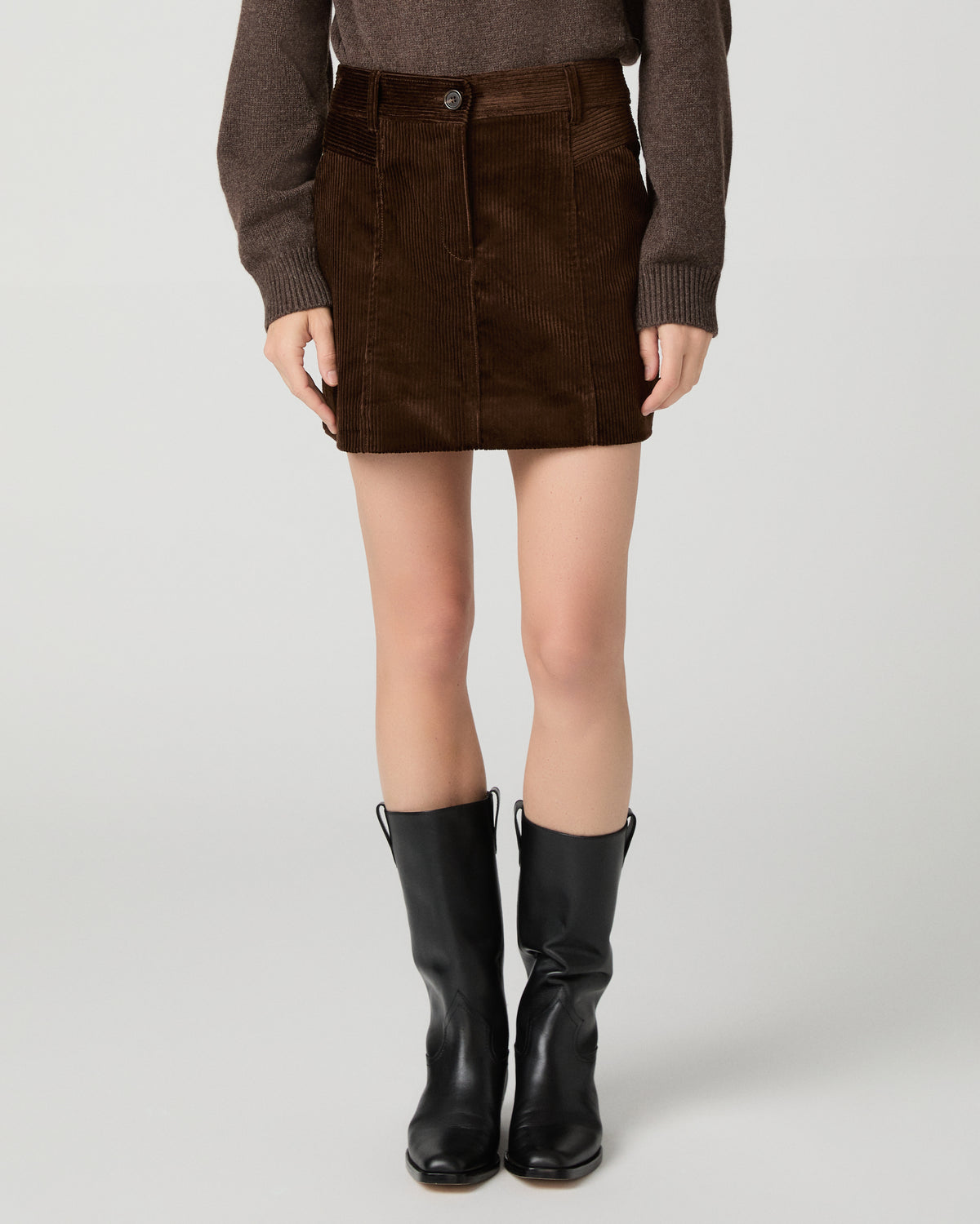 Women wearing a brown sweater and brown skirt, paired with black boots against a white background