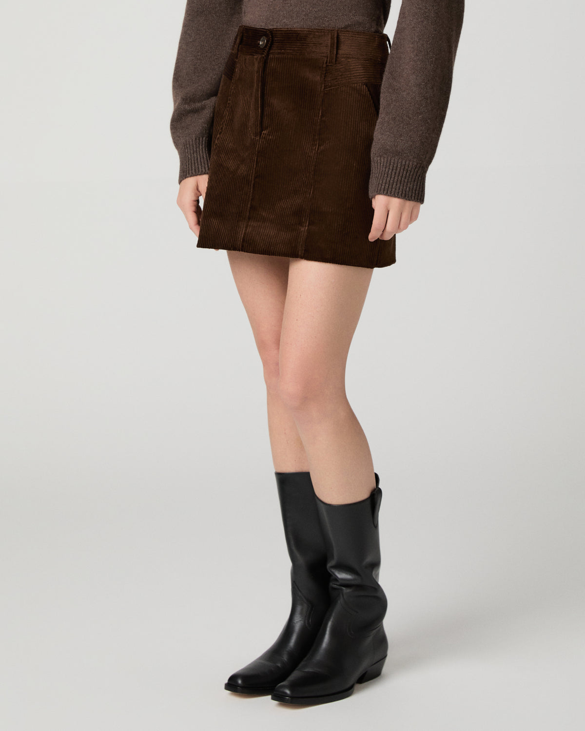 Women wearing a brown sweater and brown skirt, paired with black boots against a white background