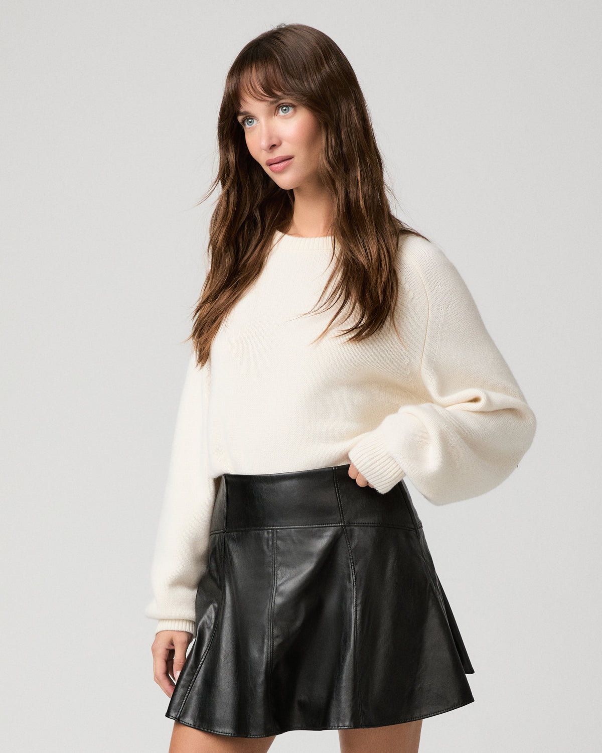 Woman wearing a white top paired with black shiny skirt against a white background