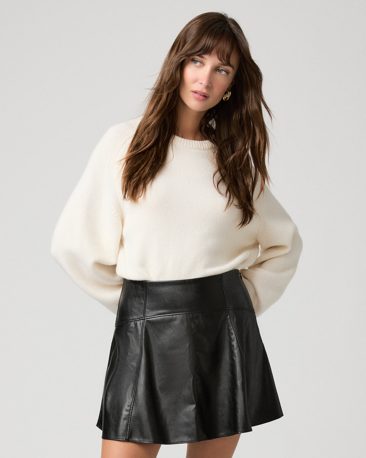Woman wearing a white top paired with black shiny skirt against a white background