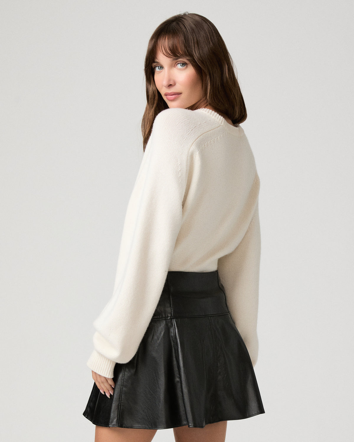 Woman wearing a white top paired with black shiny skirt against a white background