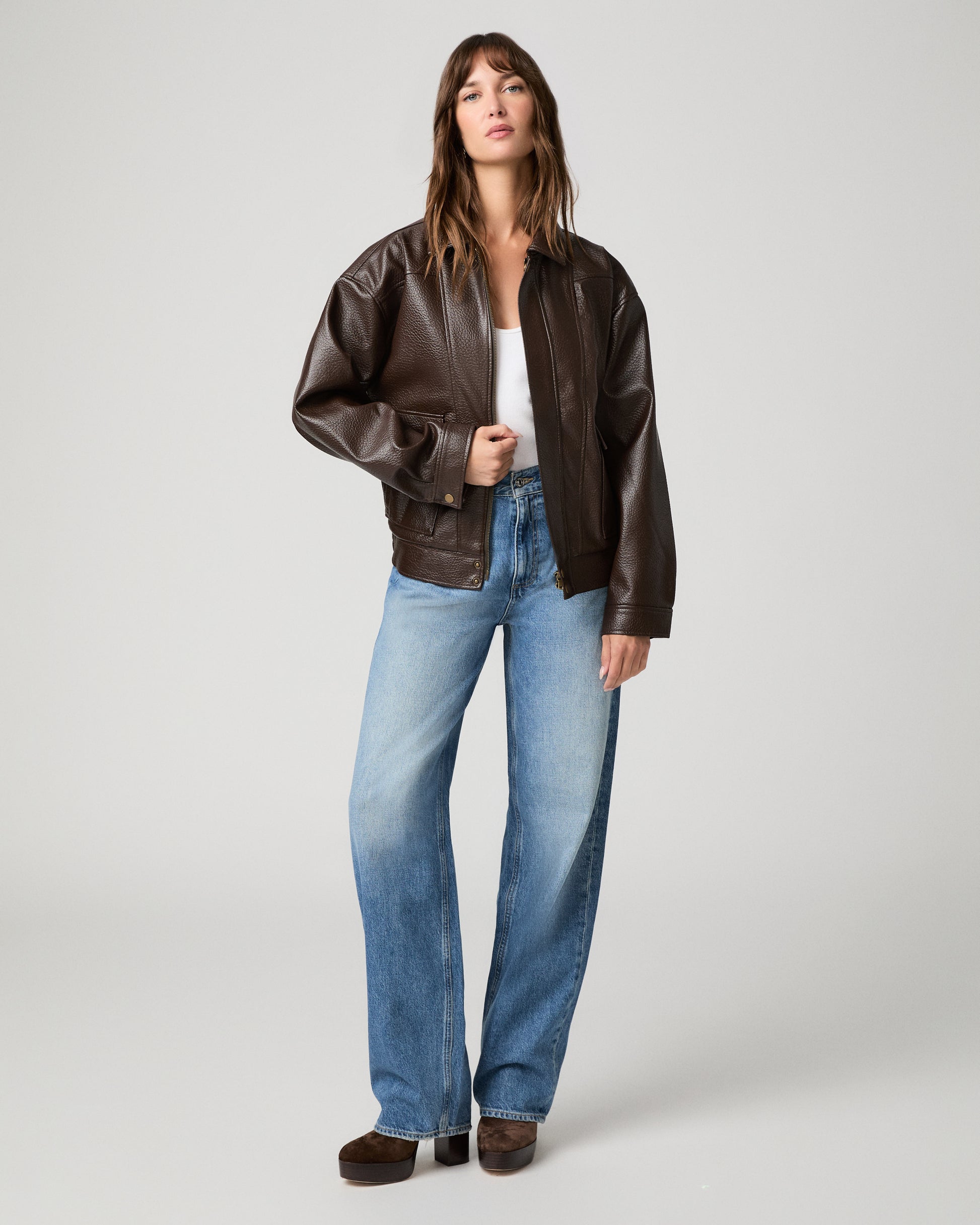 Woman wearing a white top paired with brown jacket and light pants against a white background
