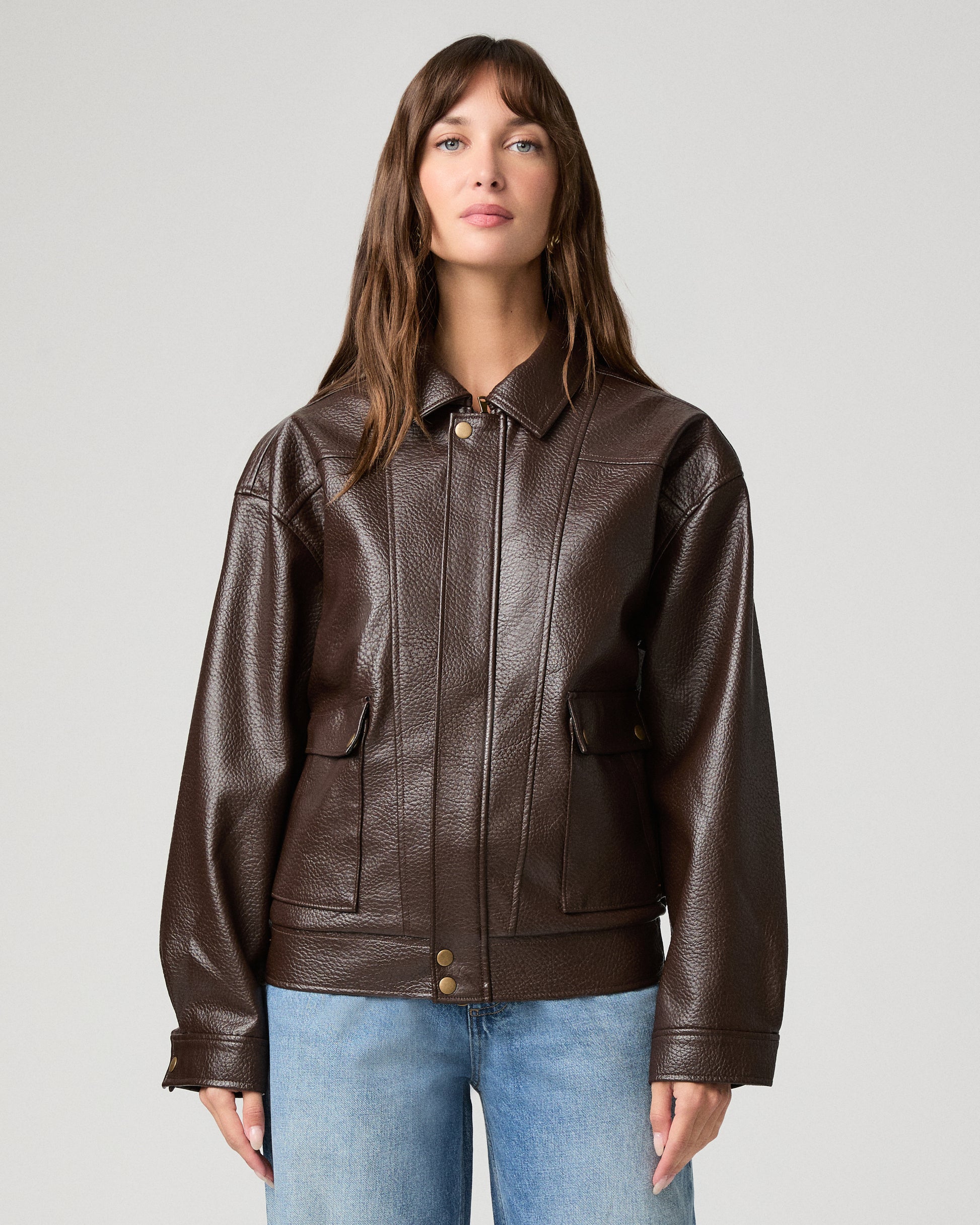 Woman wearing a brown jacket and light pants against a white background