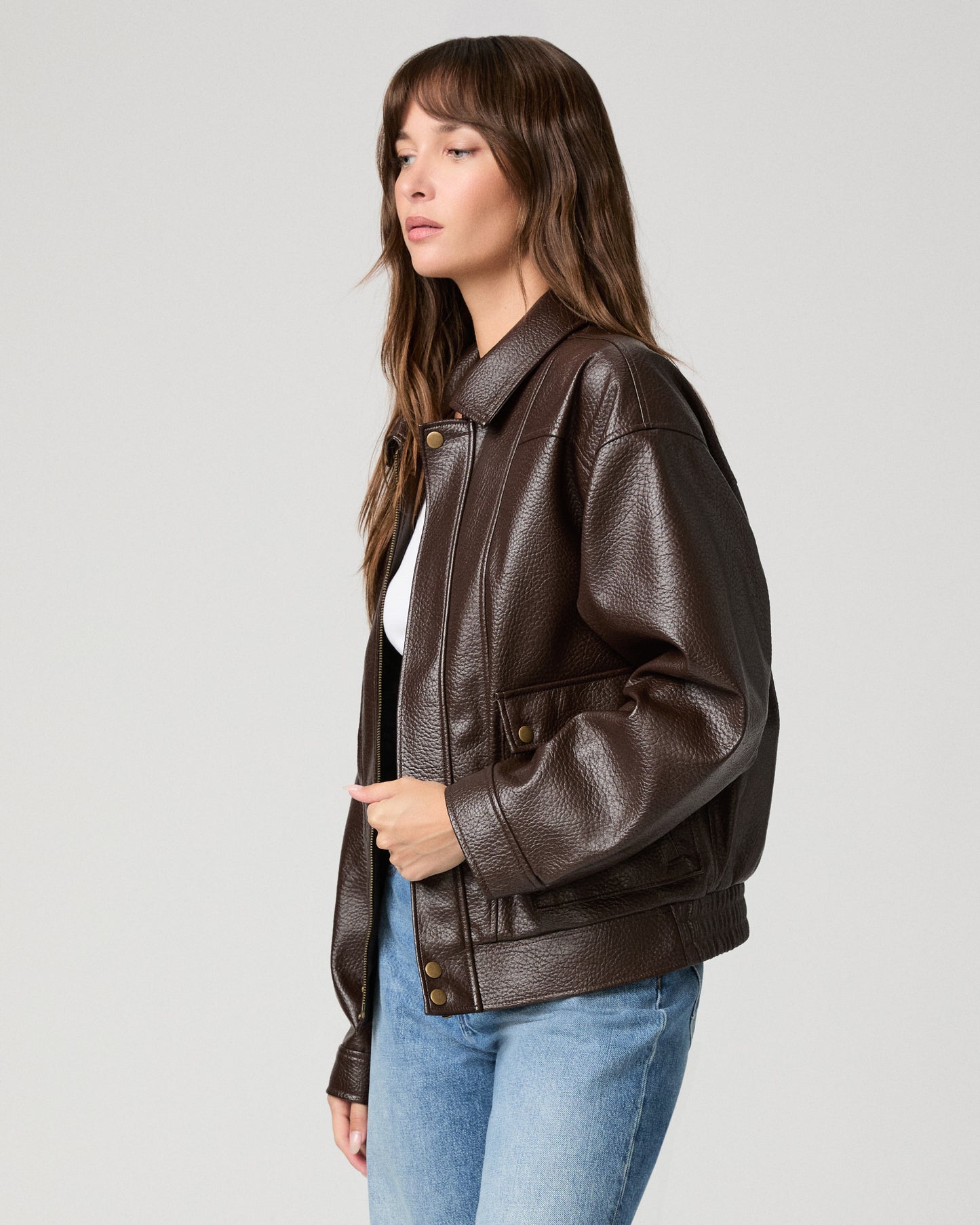 Woman wearing a white top paired with brown jacket and light pants against a white background