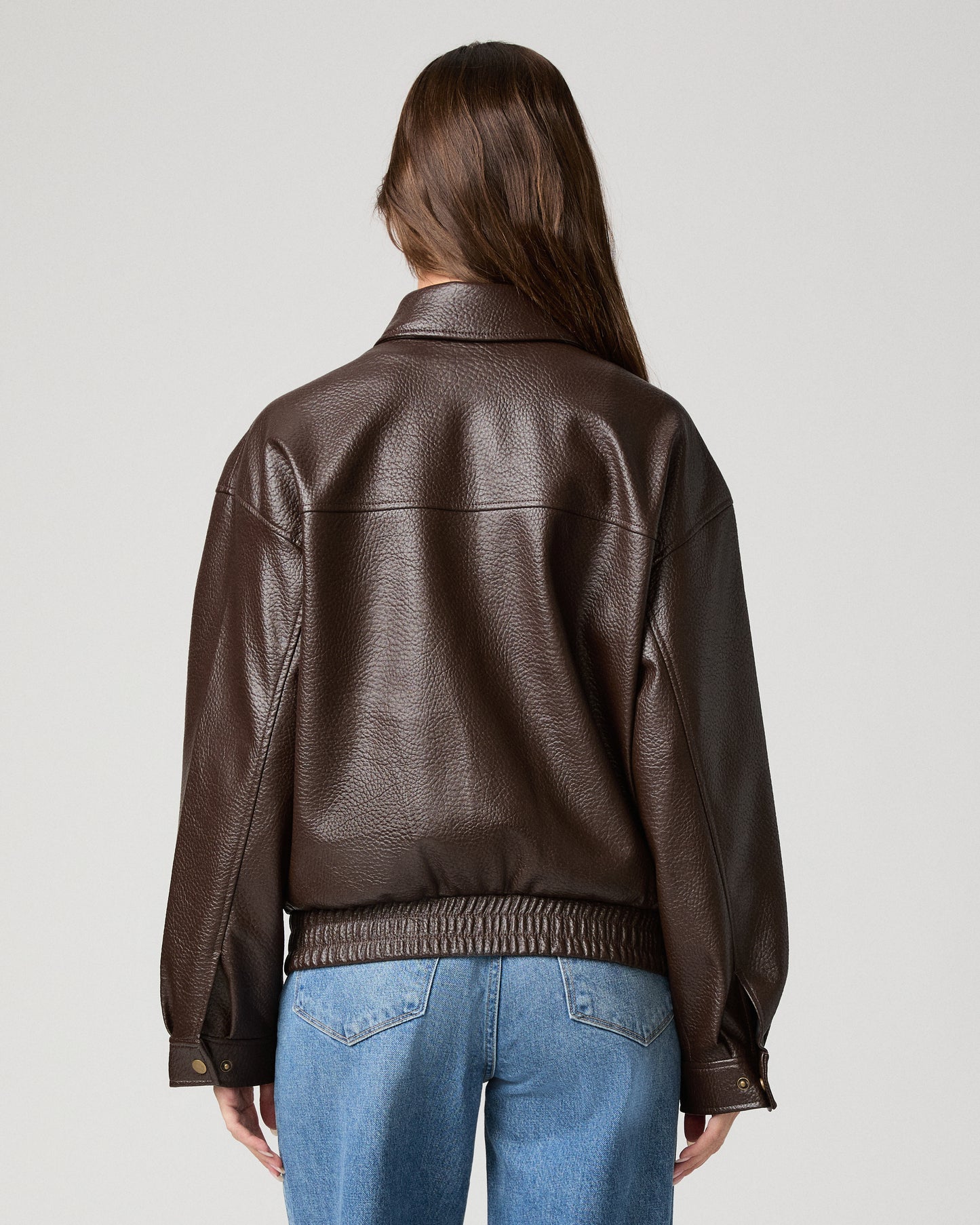 Woman wearing a brown jacket and light pants against a white background
