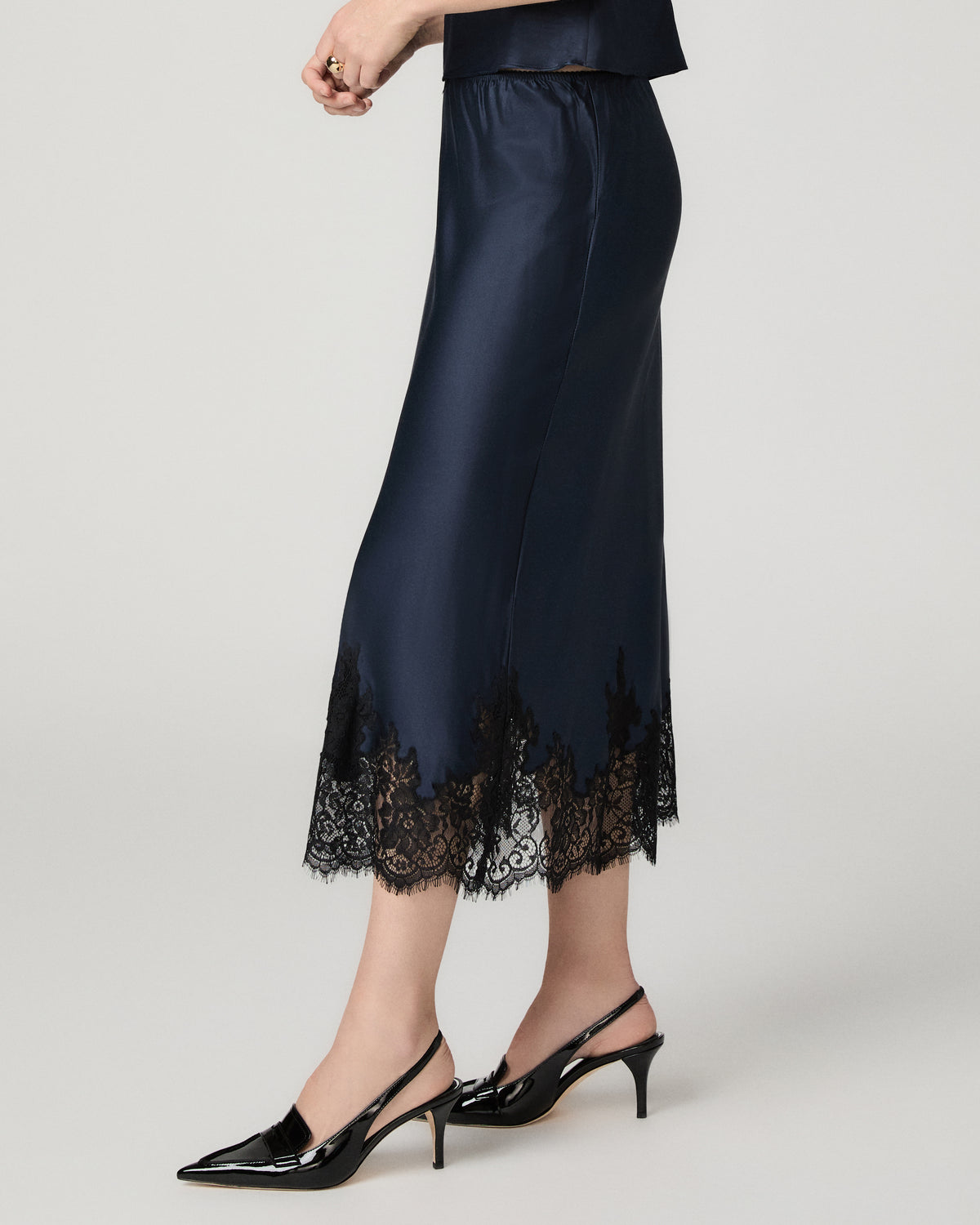 Close-up side view of the navy satin Kelso Skirt's lace hem, paired with black slingback heels.